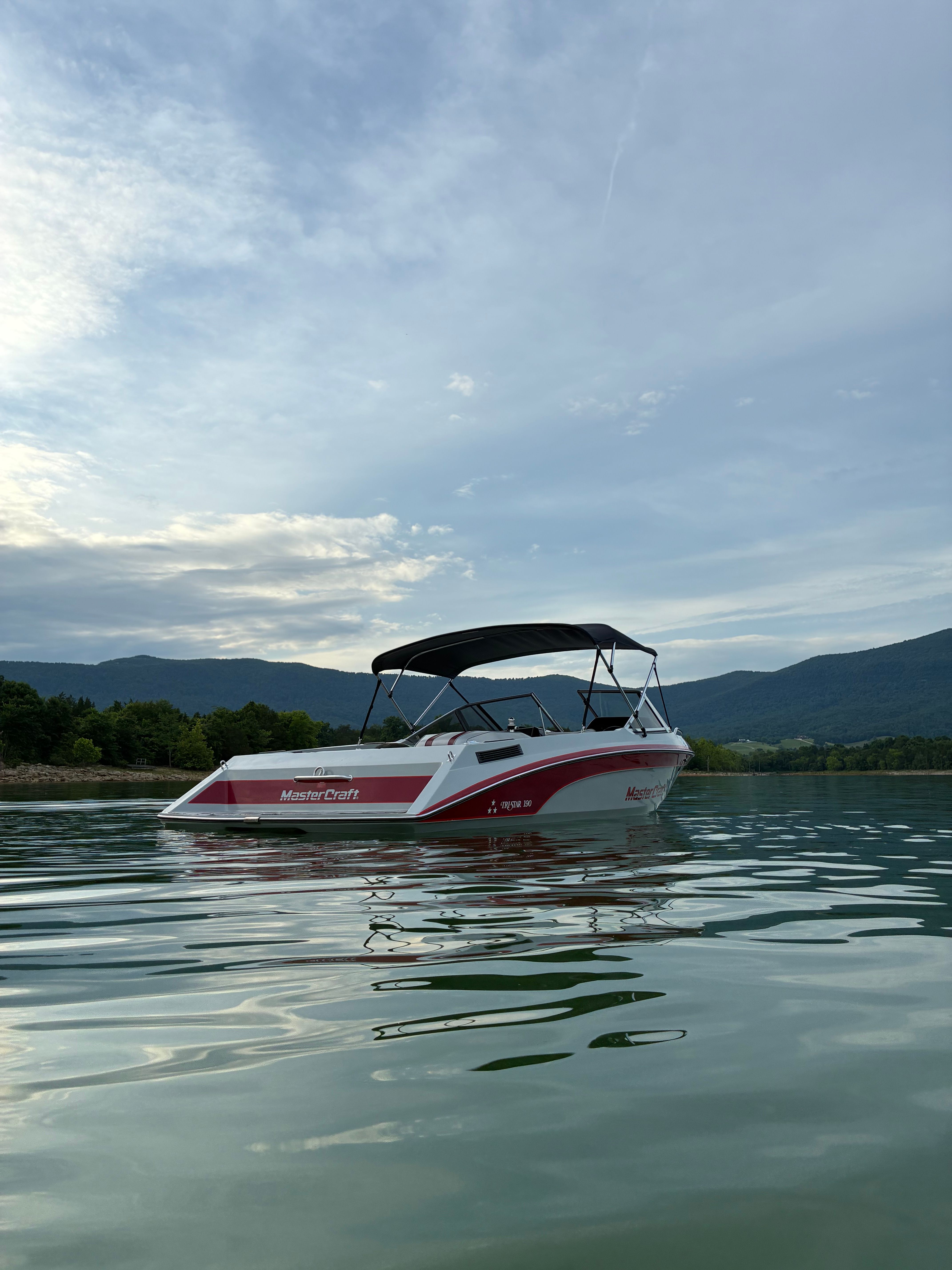 A 1989 MasterCraft TriStar 190 floats on calm water near a wooded shoreline.