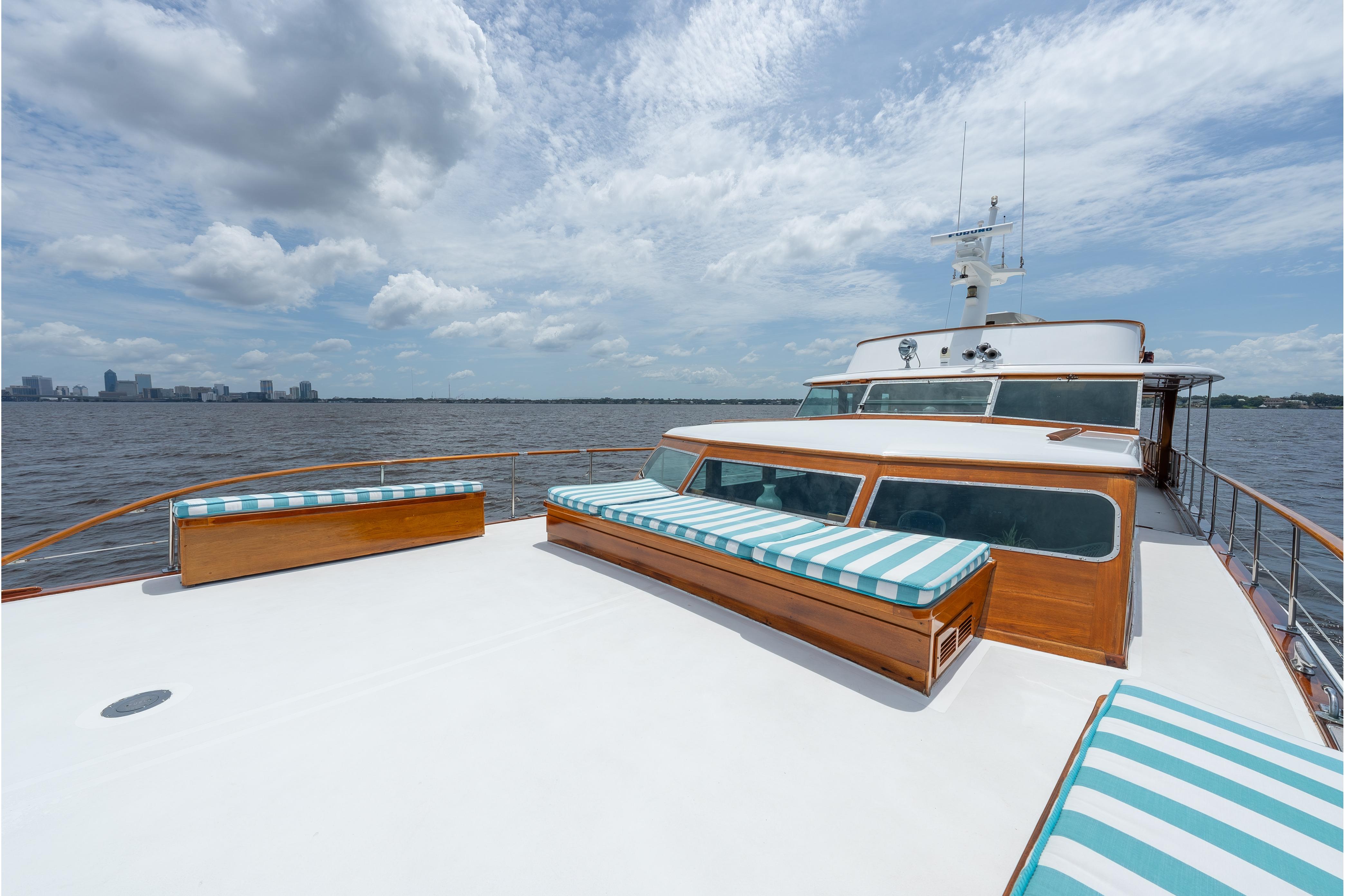 1963 Trumpy Classic yacht deck with striped cushions, overlooking a serene waterfront cityscape.