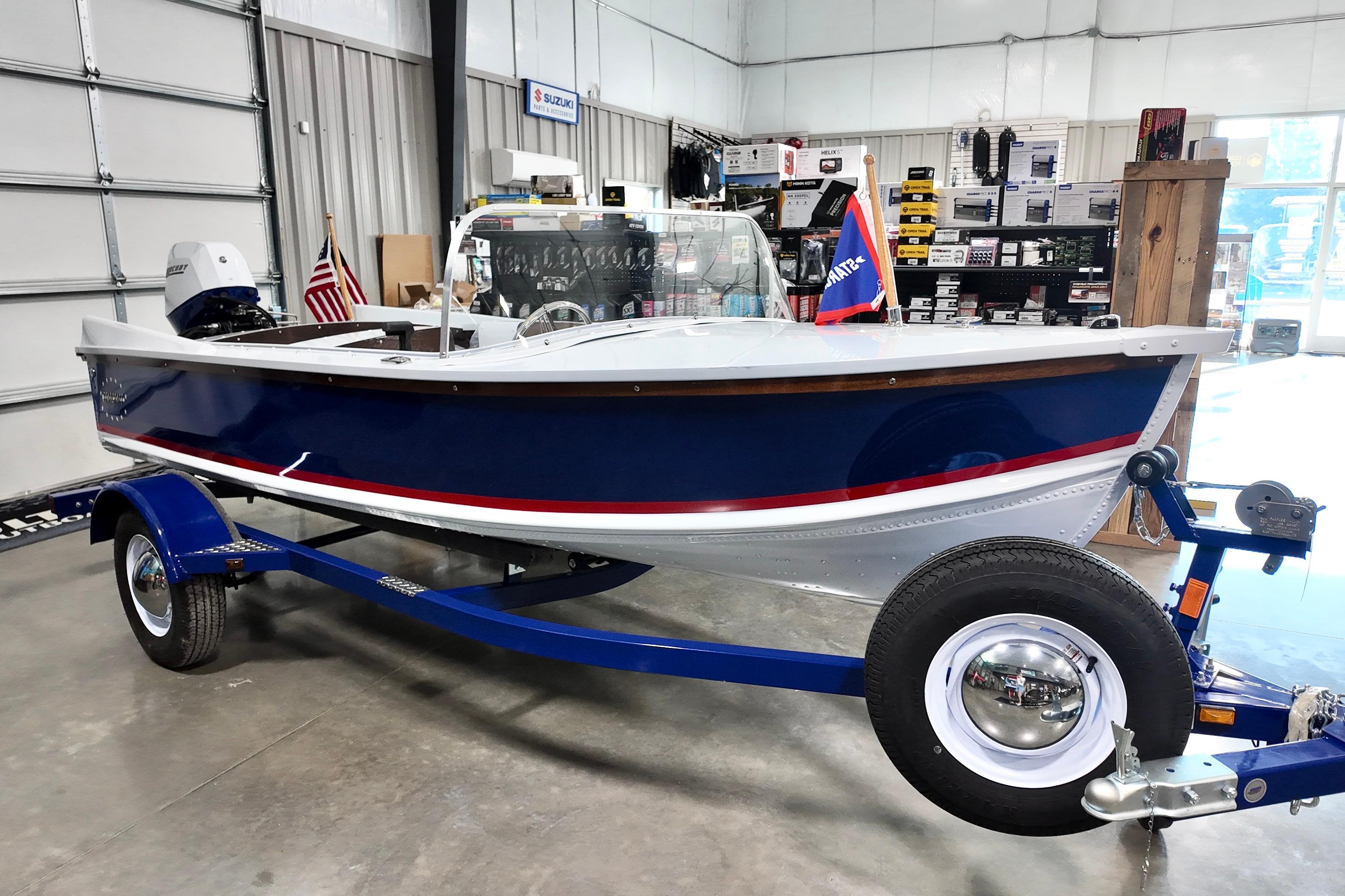 2026 Starcraft 57 Ski Champ boat on trailer in showroom, featuring blue and white design.