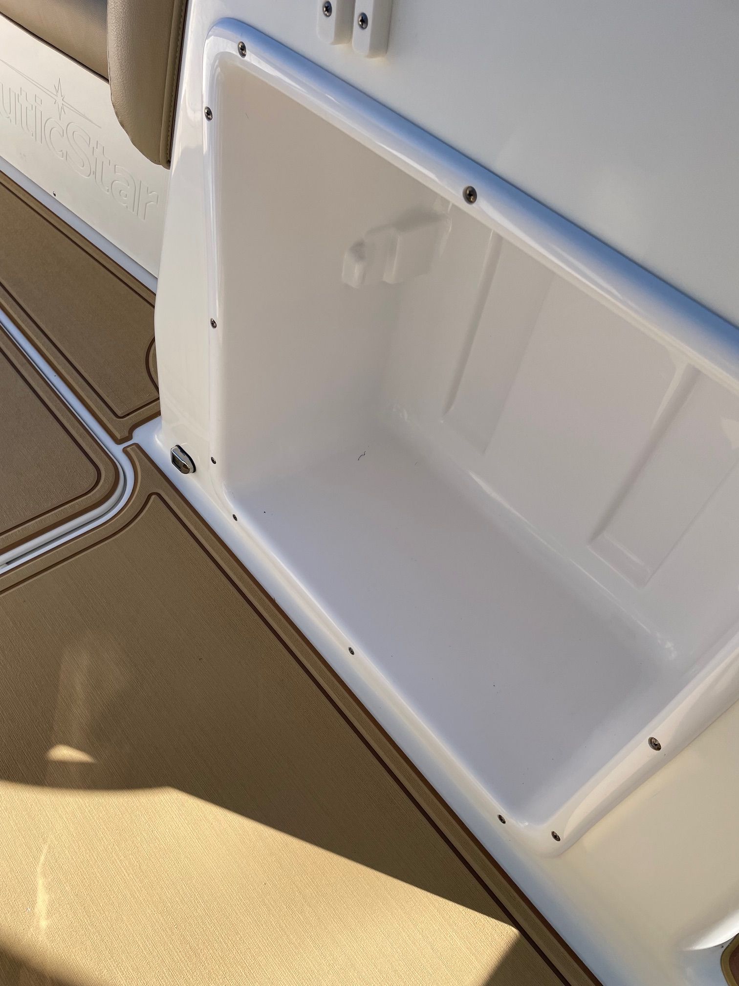 Interior view of a NauticStar 243DC Sport Deck with storage compartment and cushioned seating.
