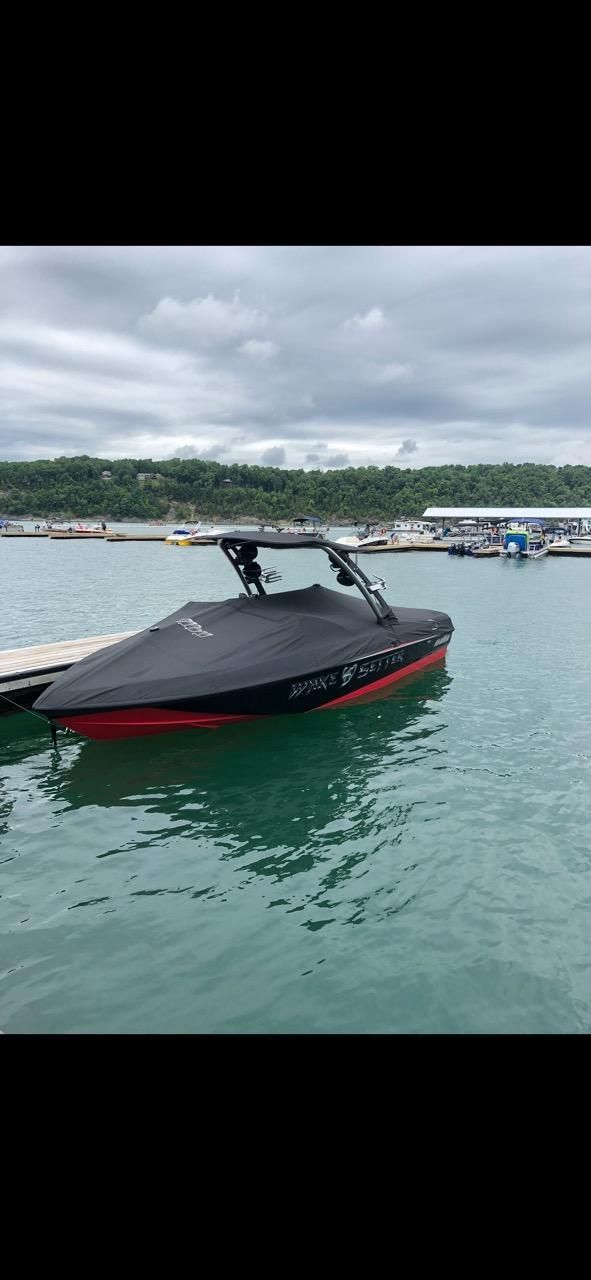 A black and red boat is on the water, surrounded by green hills and a cloudy sky.