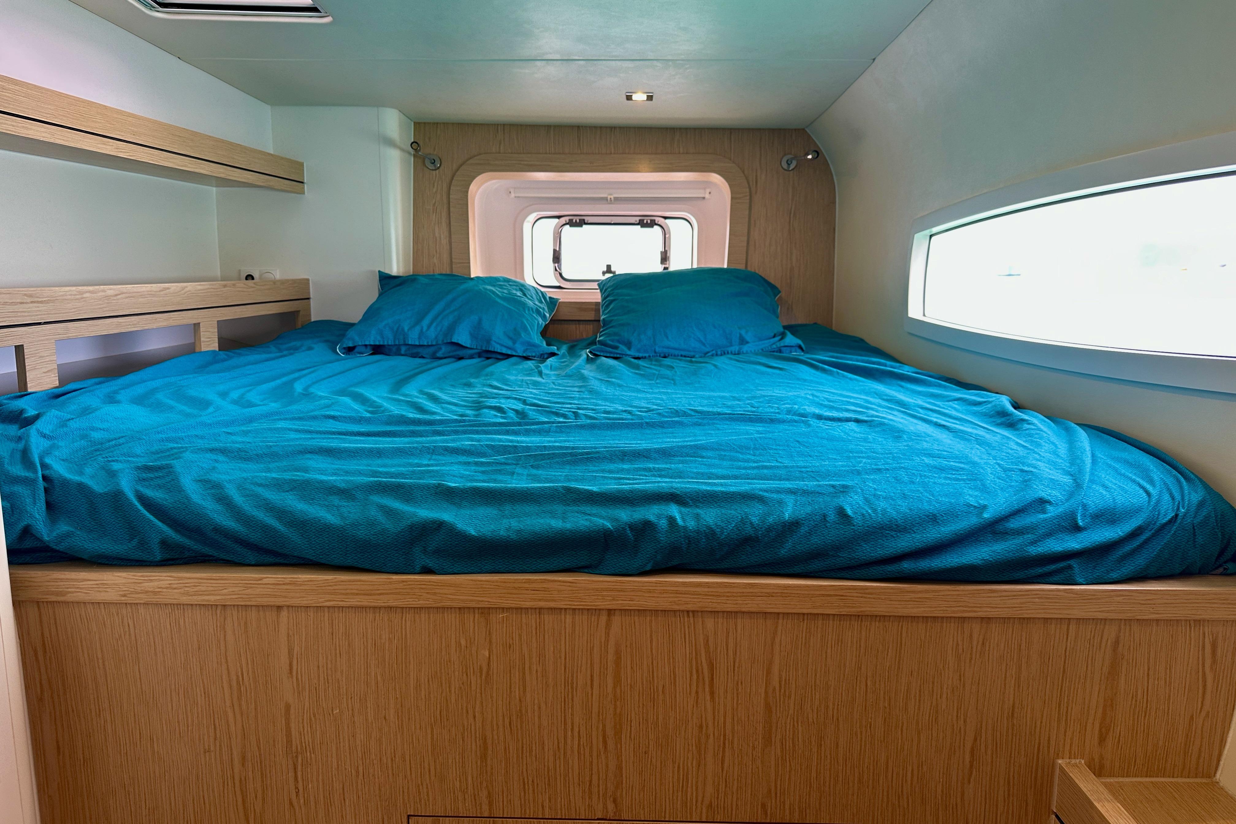 Cozy cabin bedroom in 2023 Outremer 51 yacht with blue bedding and wooden accents.