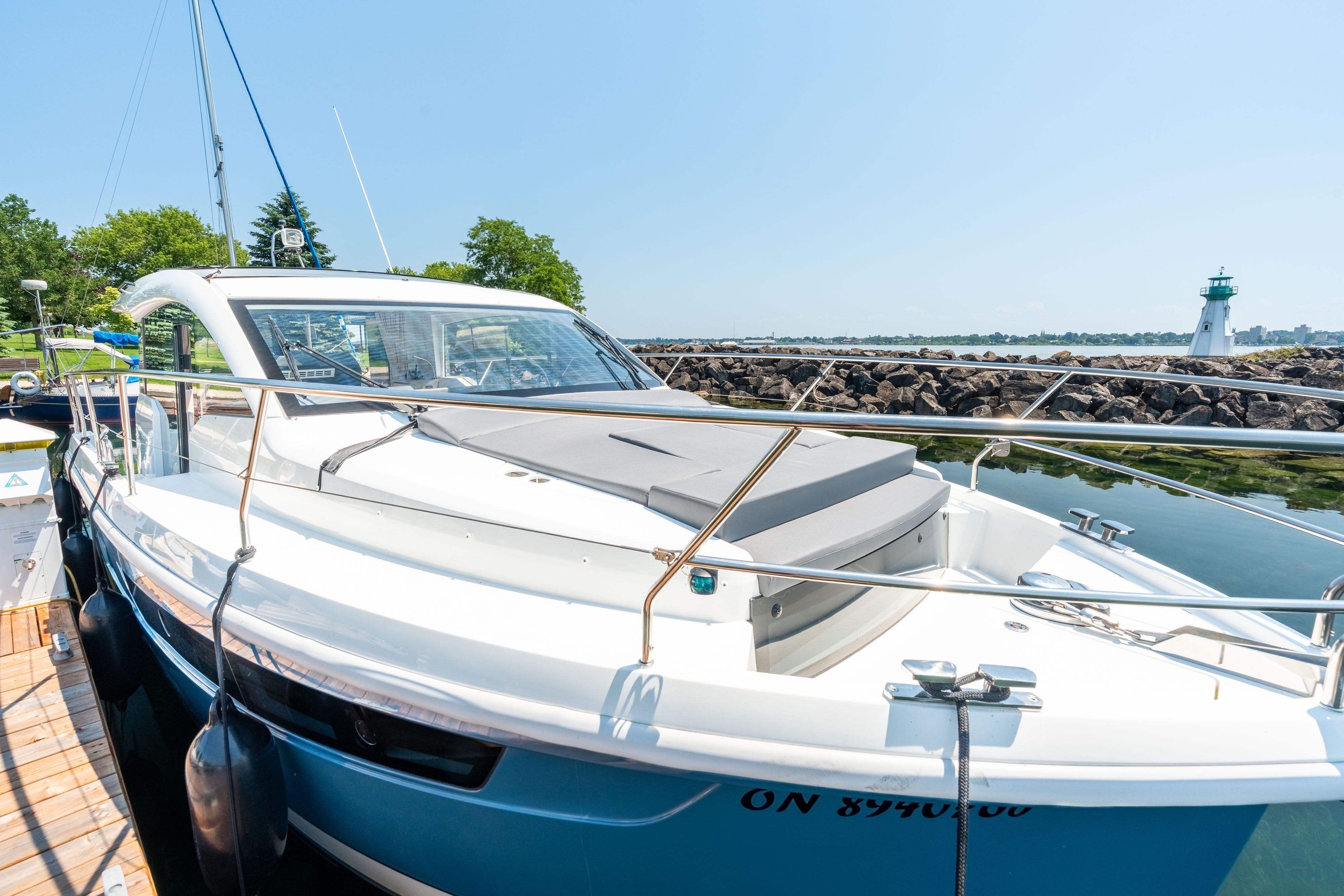 A modern Sealine C335V yacht docked with a lighthouse in the background.