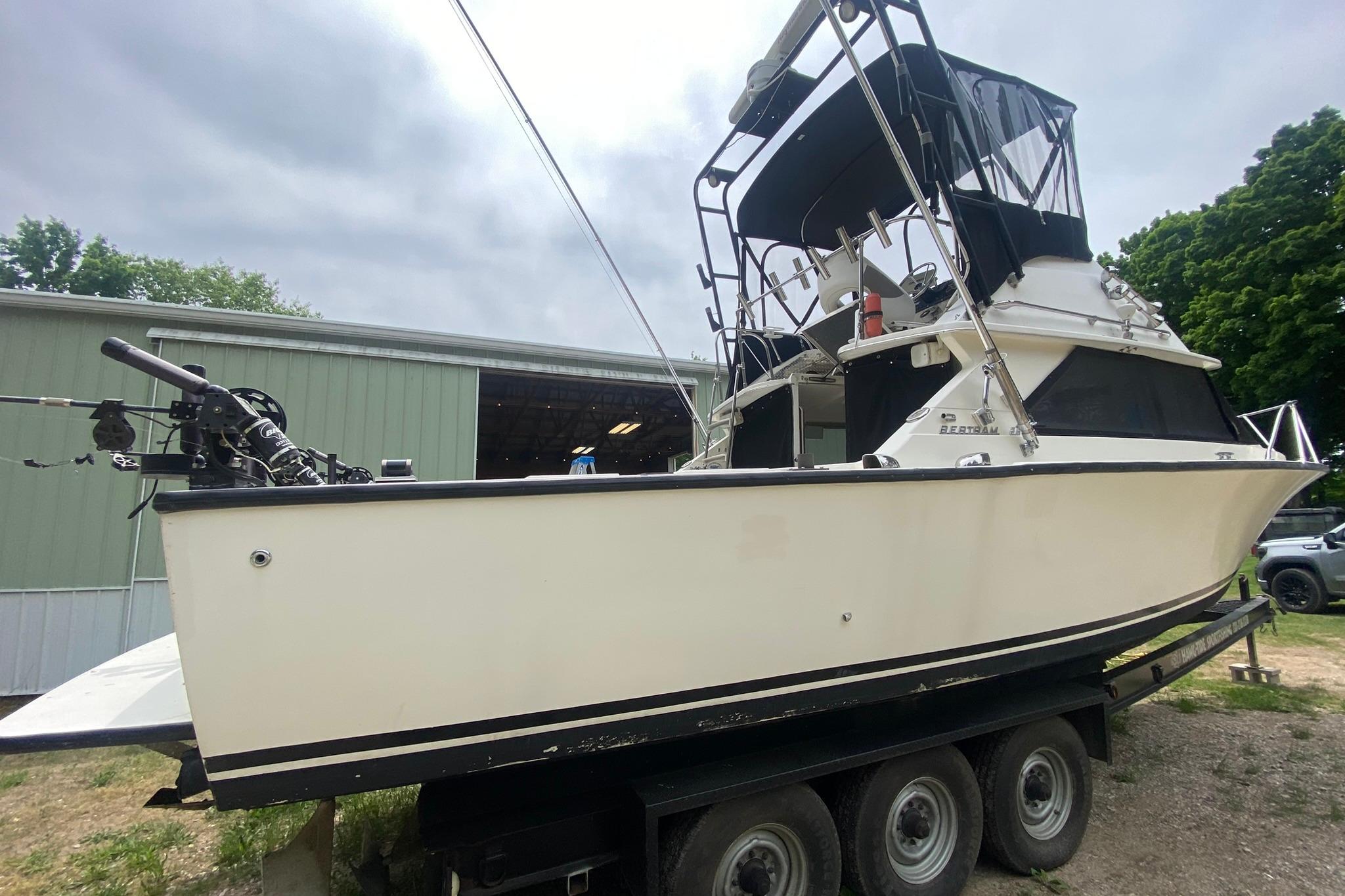 1977 Bertram 28 Flybridge boat on trailer, parked near a green building.