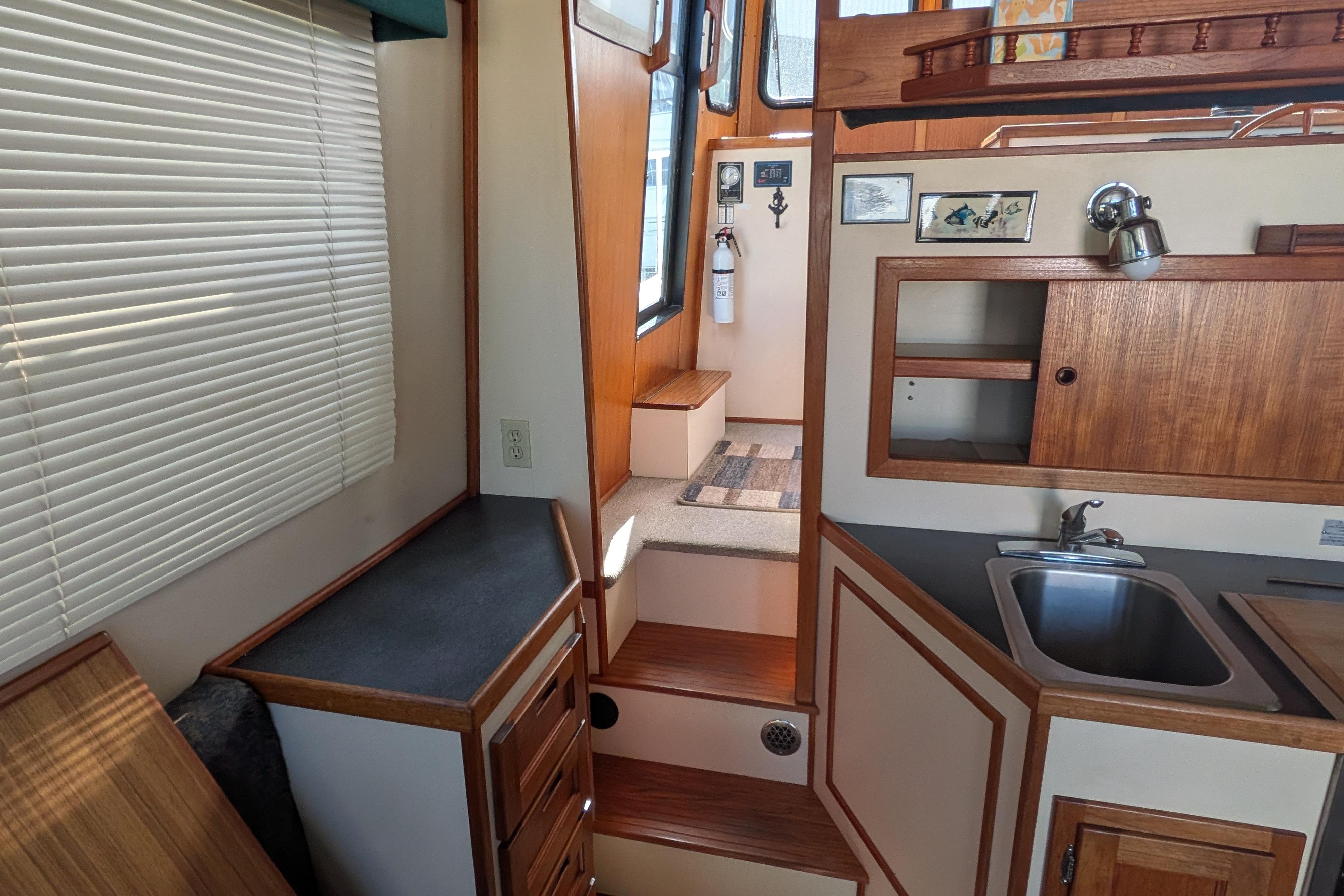 Interior of a 1998 Nordic Tug 32, featuring a compact kitchen and wooden cabinetry.
