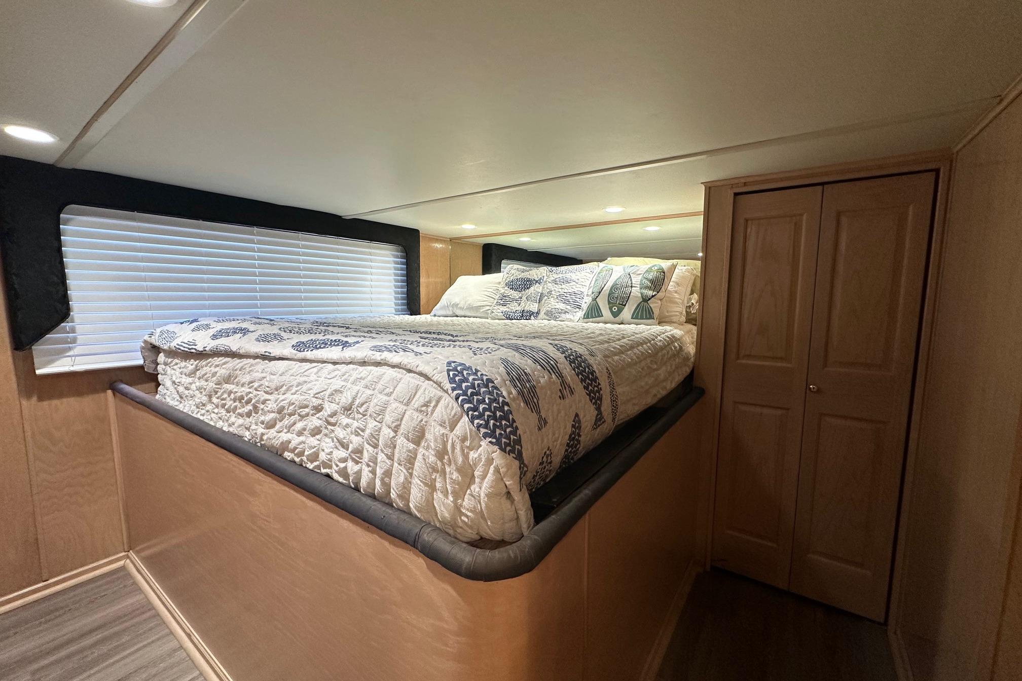 Cozy bedroom in 1999 Sumerset 18x94 houseboat with elevated bed and wooden closet.