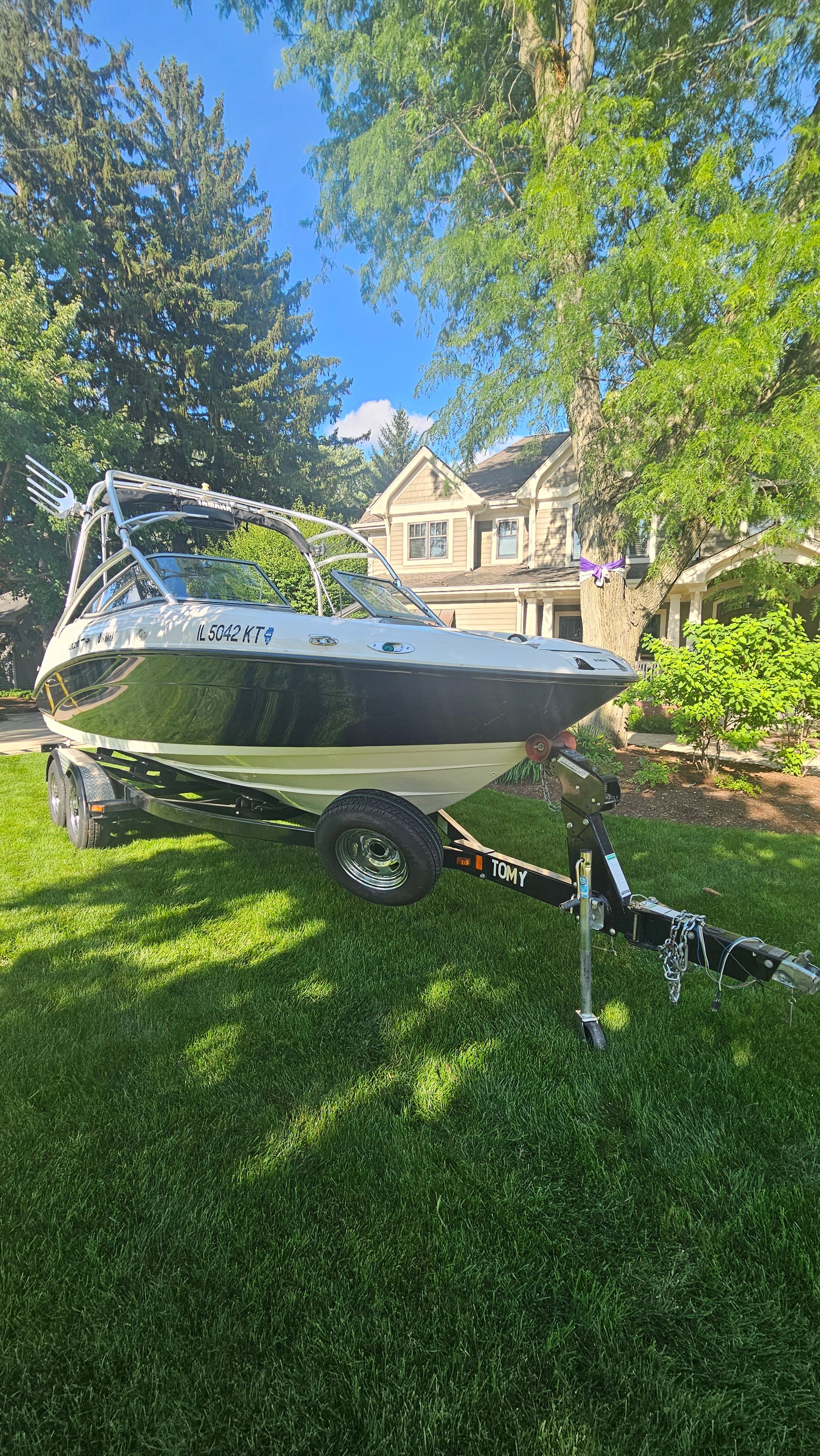 A 2010 Yamaha AR210 boat on a trailer in a green garden setting.