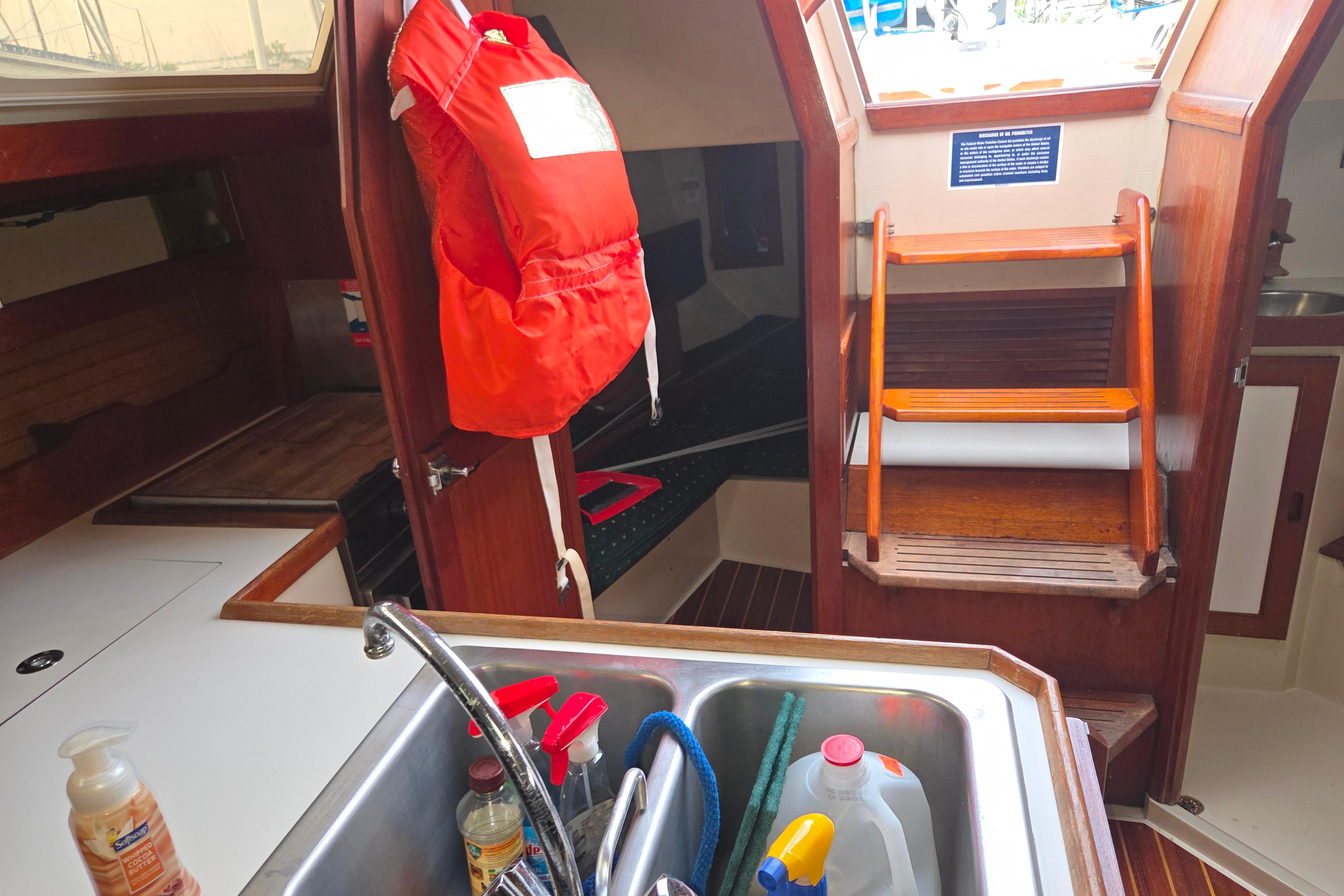 Interior of 1986 Catalina 355 sailboat with sink, life jacket, and wooden steps.