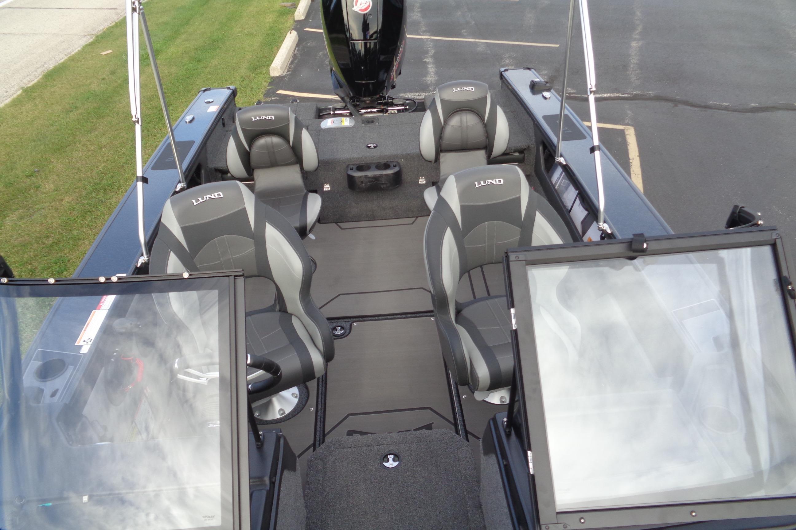 2026 Lund 1875 Crossover XS boat interior with seating and windshield, parked on pavement.