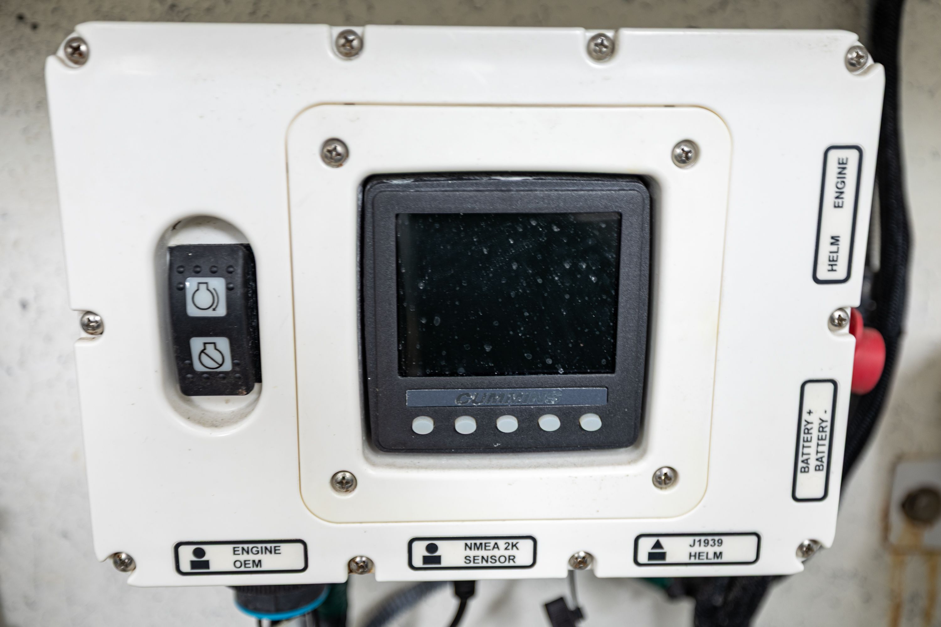 A control panel with a screen and switches, surrounded by cables, inside a boat.