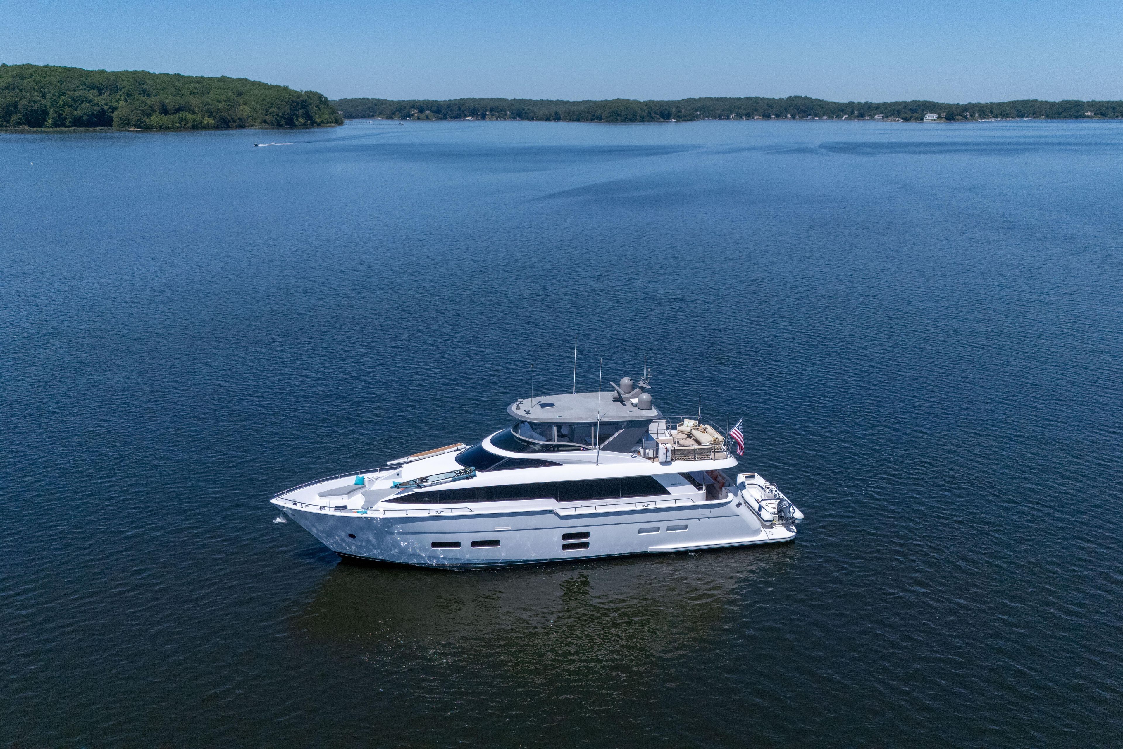 2021 Hatteras M75 Panacera yacht cruising on a serene lake under clear blue skies.