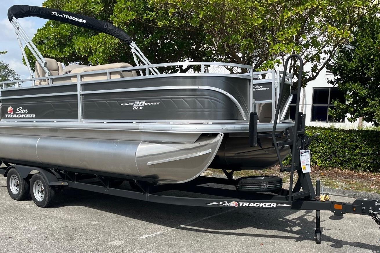 2025 Sun Tracker Fishin' Barge 20 DLX pontoon boat on trailer, parked outdoors.