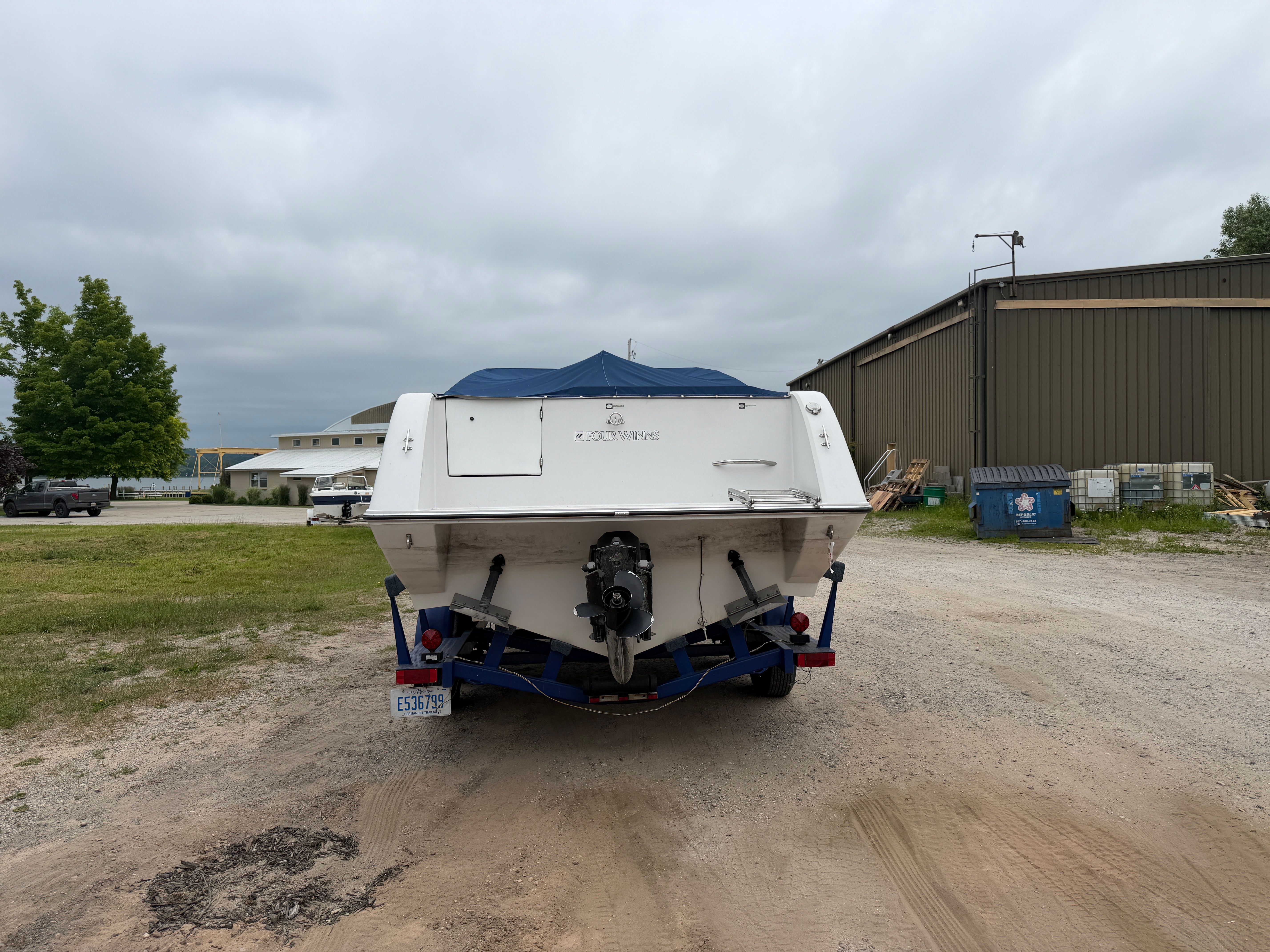 A 1992 Four Winns 225 Sundowner on a trailer, parked on a gravel lot.