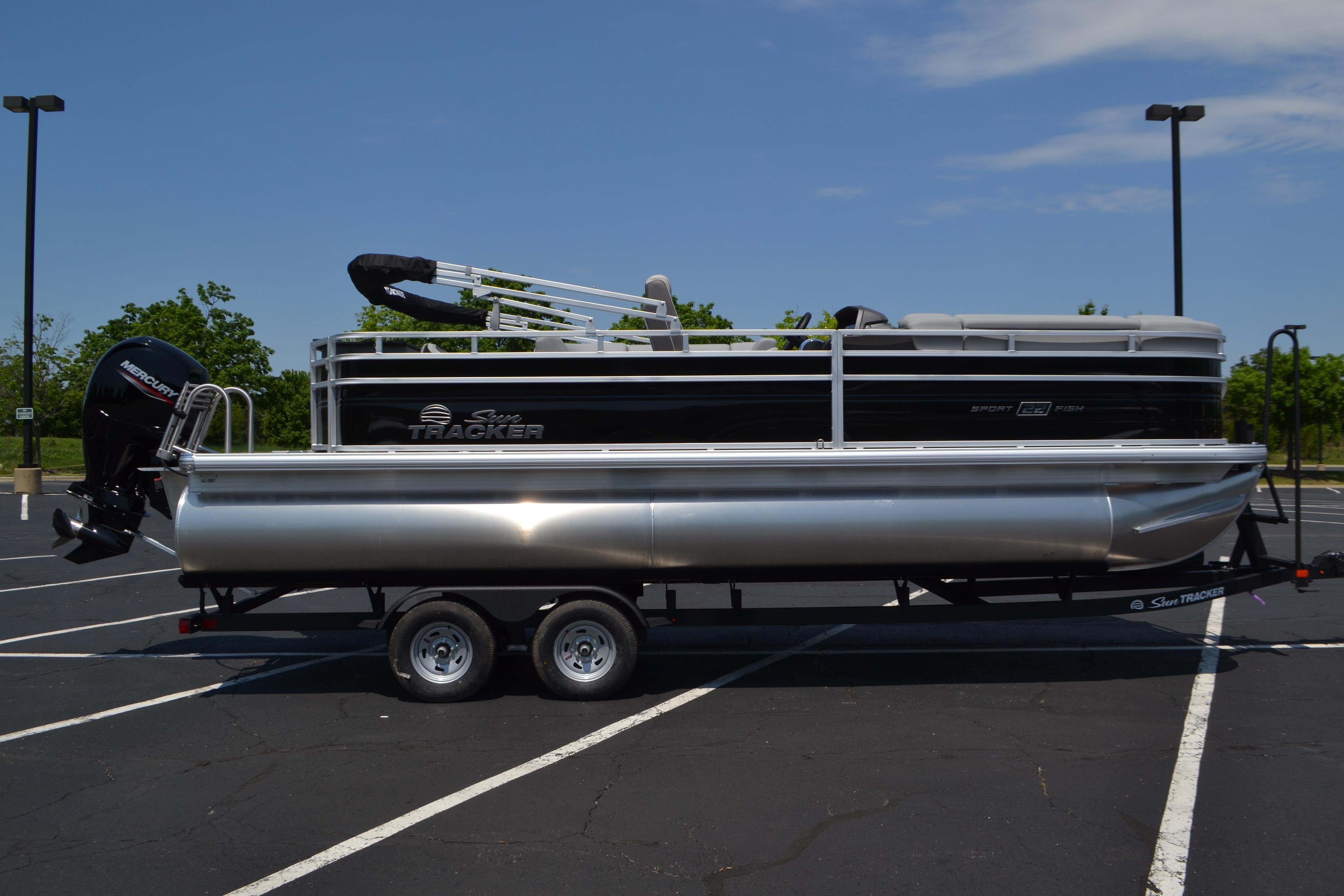 2026 Sun Tracker SportFish 22 DLX pontoon boat on trailer in parking lot.