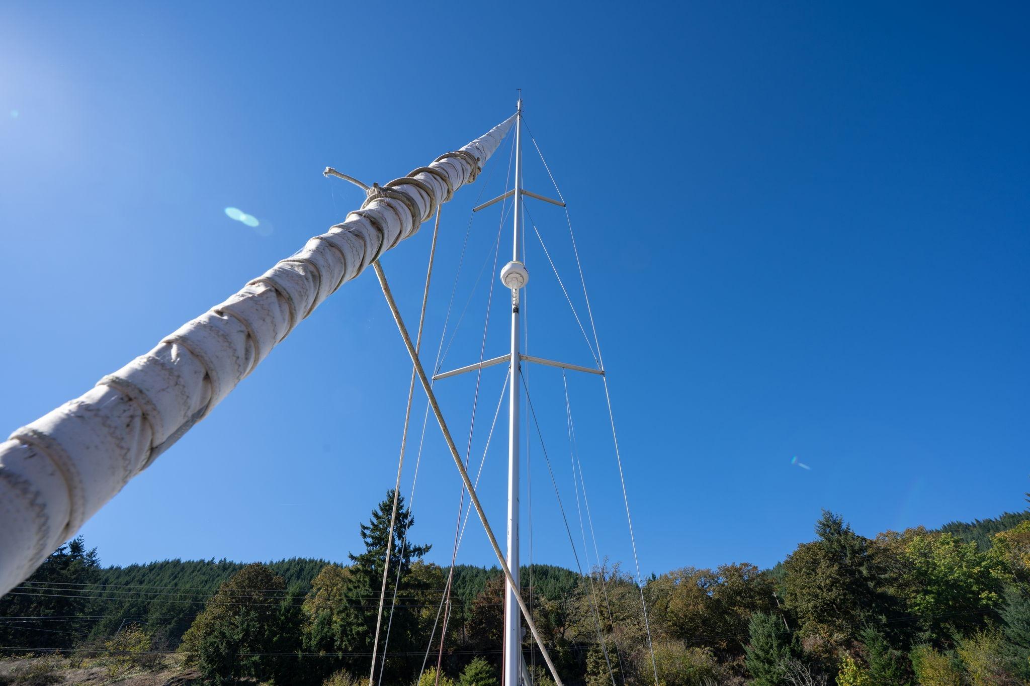 Mast of 2013 Beneteau Oceanis 50 sailboat against clear blue sky and forest backdrop.