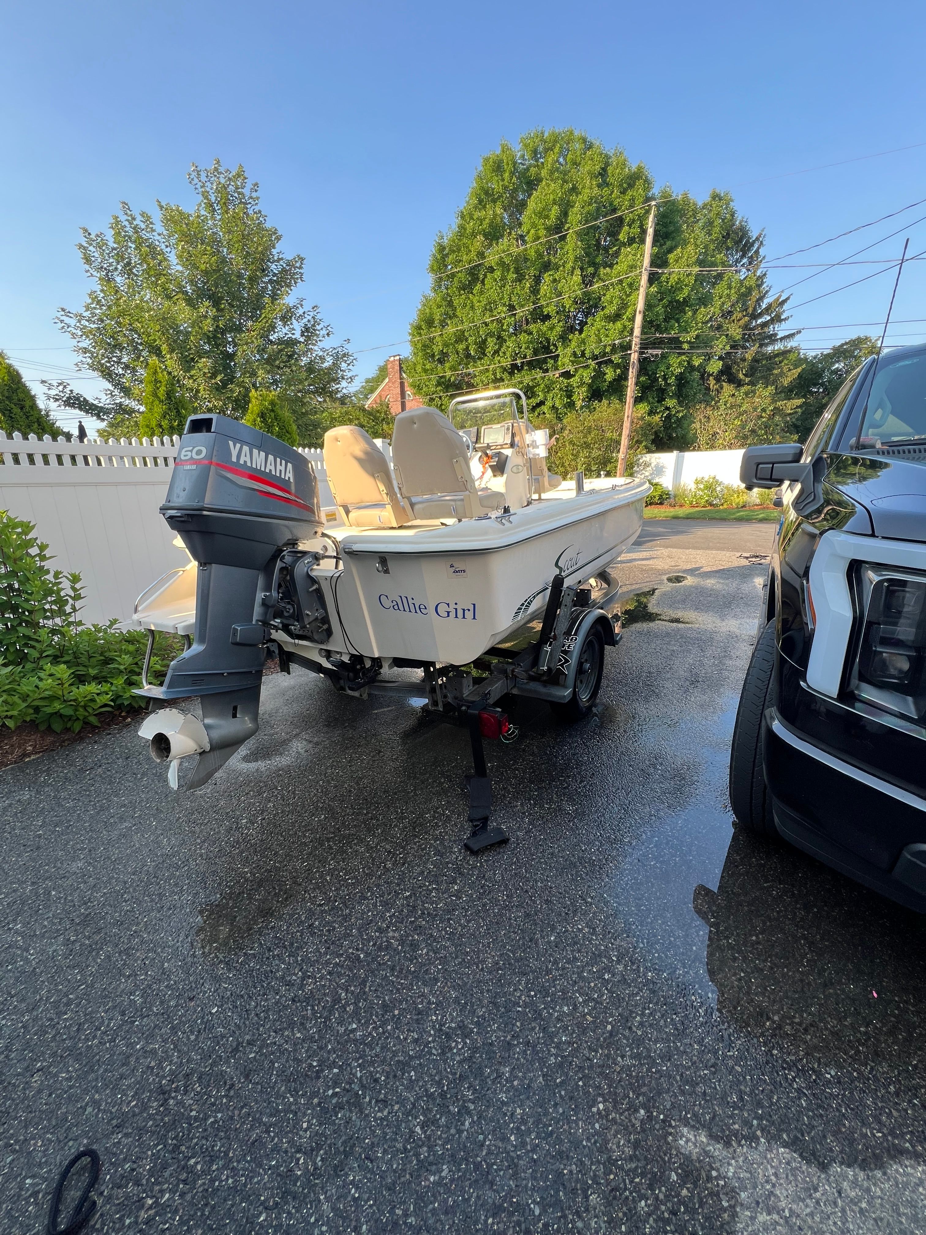 A 2001 Scout 151 Sportfish boat on a trailer next to a black vehicle.