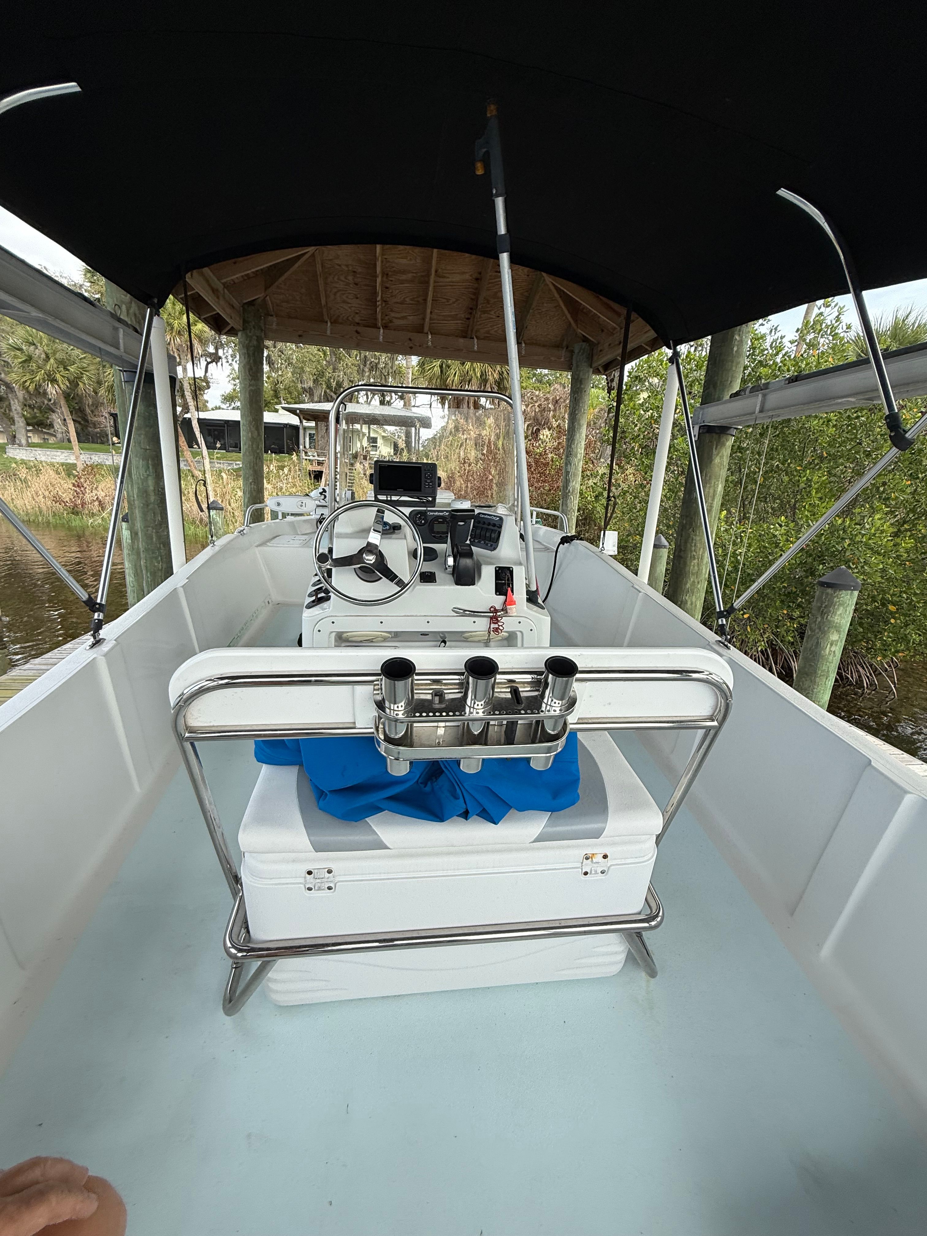 A boat with a covered helm and fishing rod holders, docked at a pier.