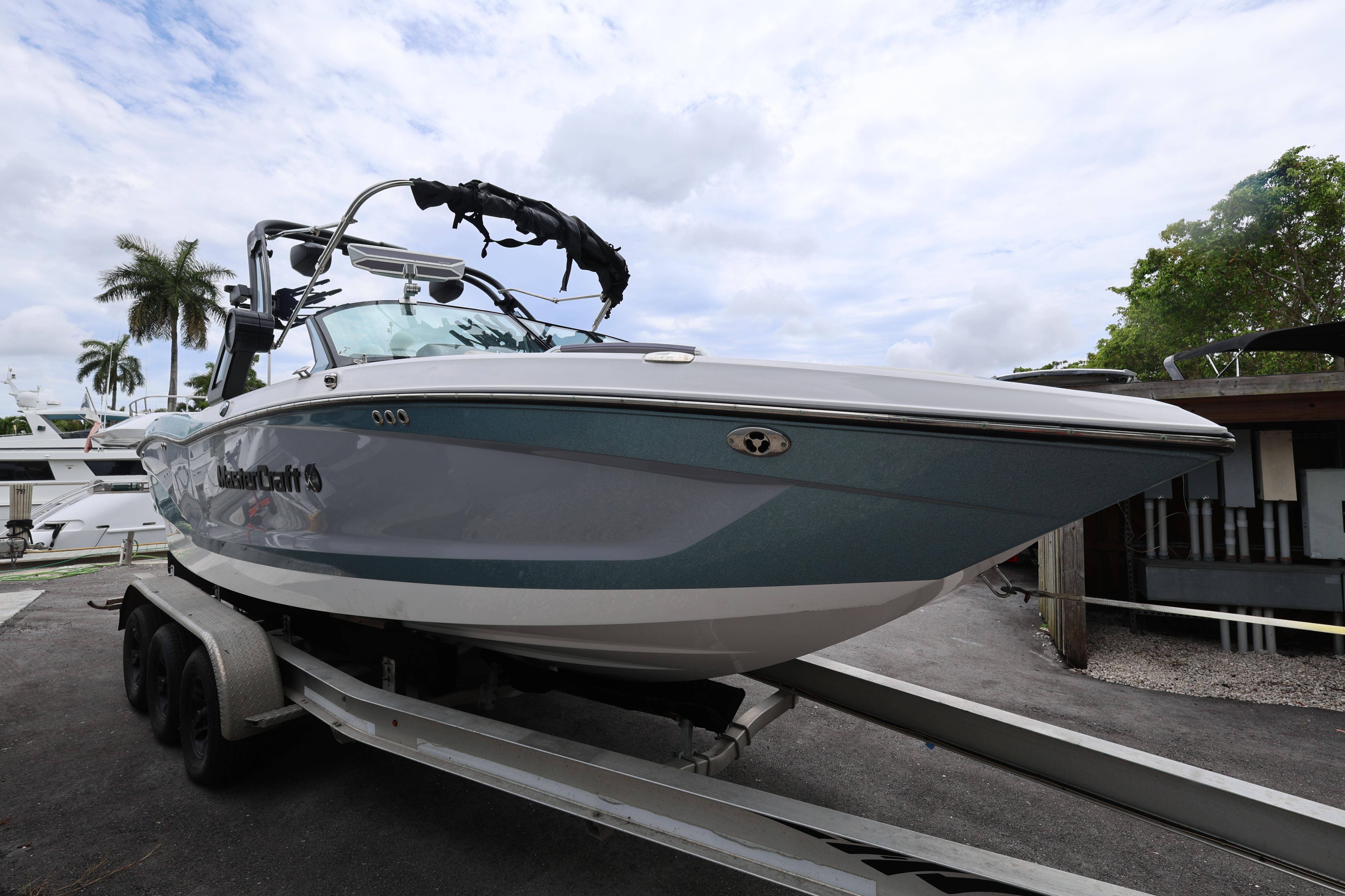 2023 MasterCraft X24 boat on trailer, parked outdoors under cloudy sky.