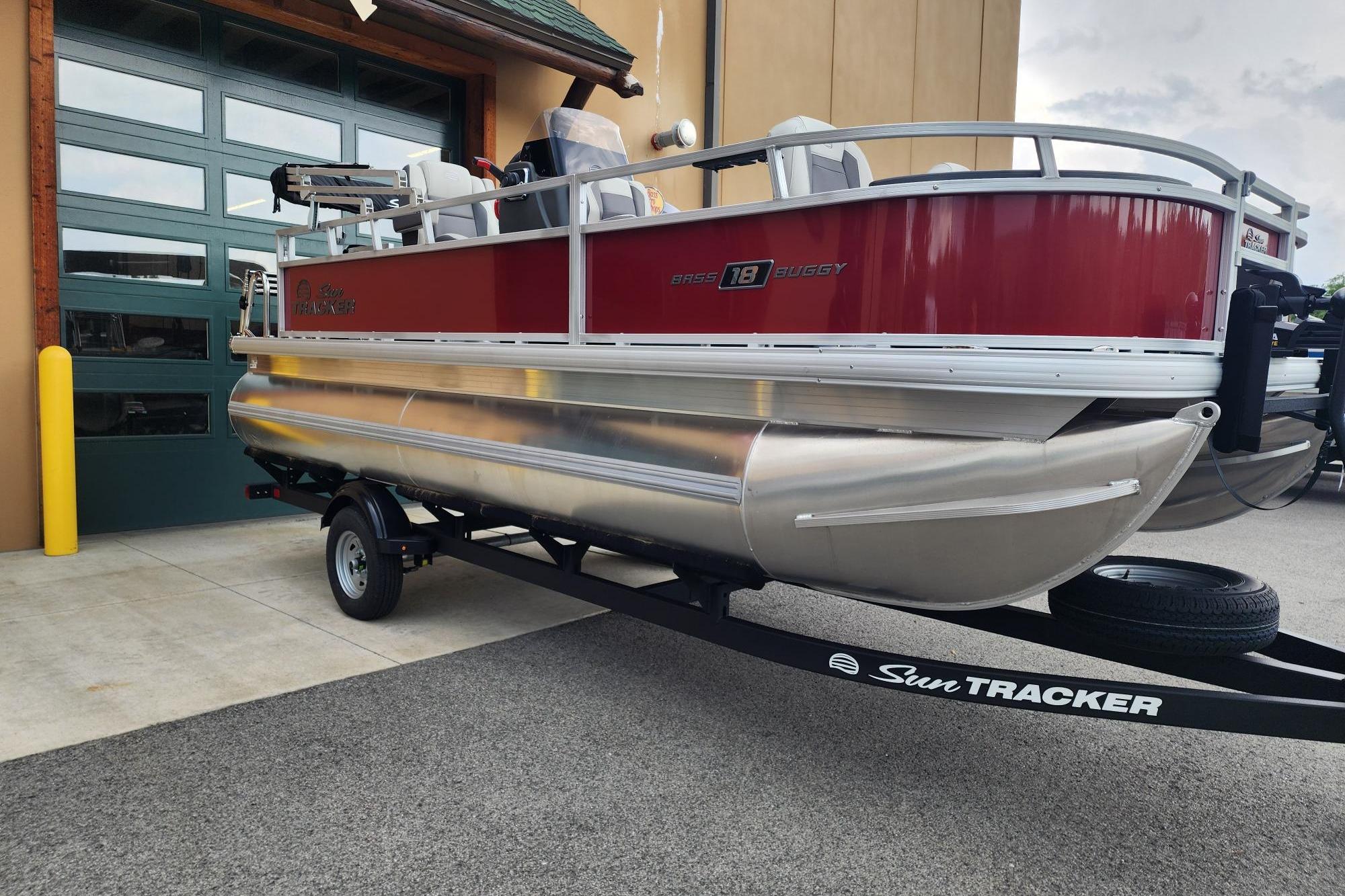 2026 Sun Tracker Bass Buggy 18 DLX pontoon boat on trailer, parked outside a garage.
