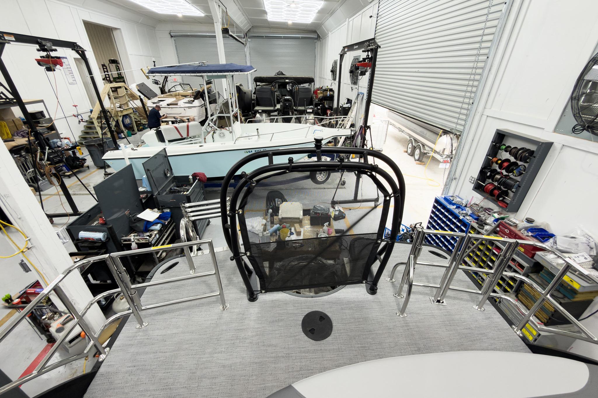 2026 Godfrey Monaco 25' Tritoon in a workshop, surrounded by tools and equipment.