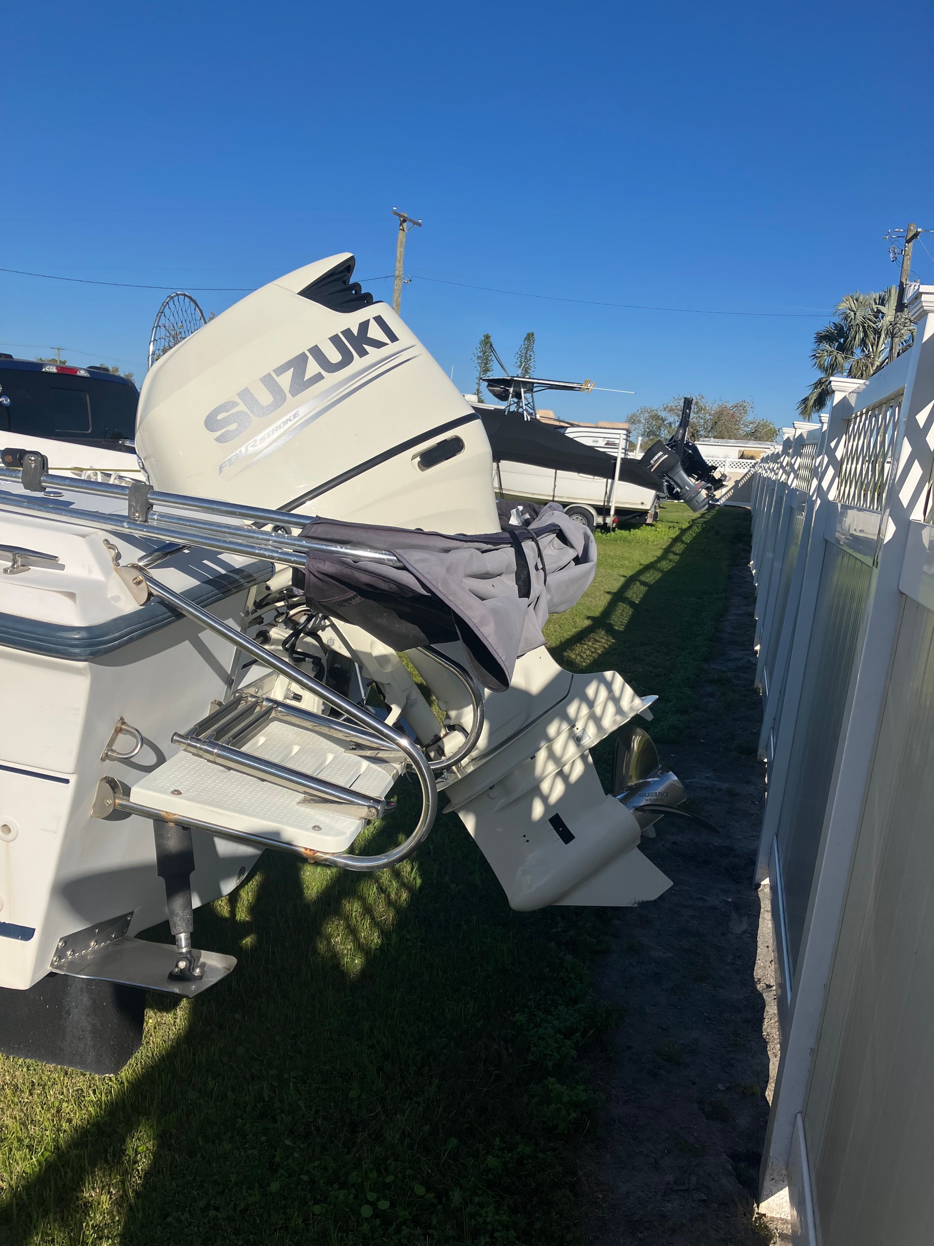 A boat with a Suzuki outboard motor is on grass next to a fence.