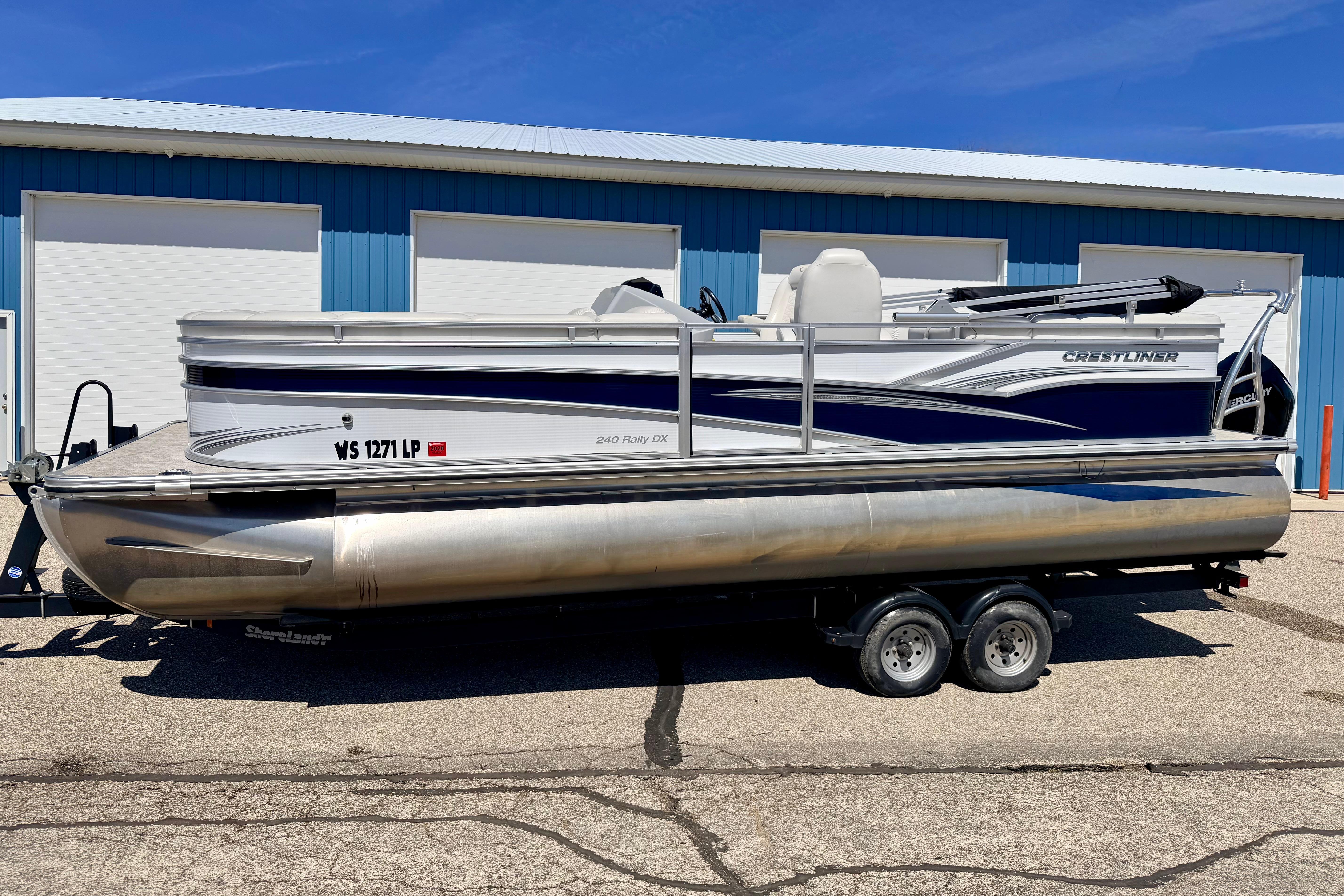 2019 Crestliner 240 Rally DX CW pontoon boat on trailer, parked outside blue building.