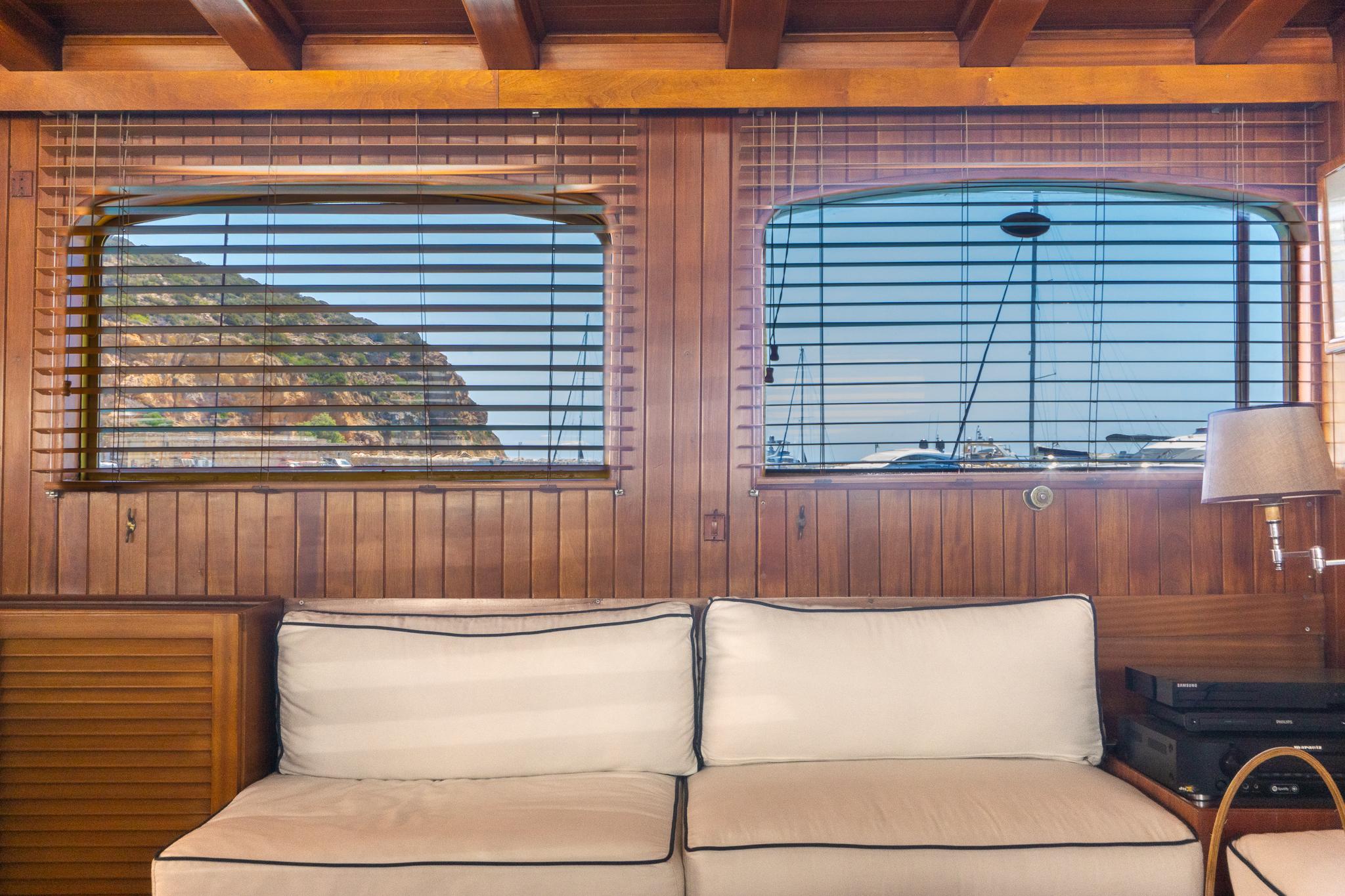 Wood-paneled yacht interior with cushioned seating, Psarros Shipyard 1969, scenic ocean view through windows.