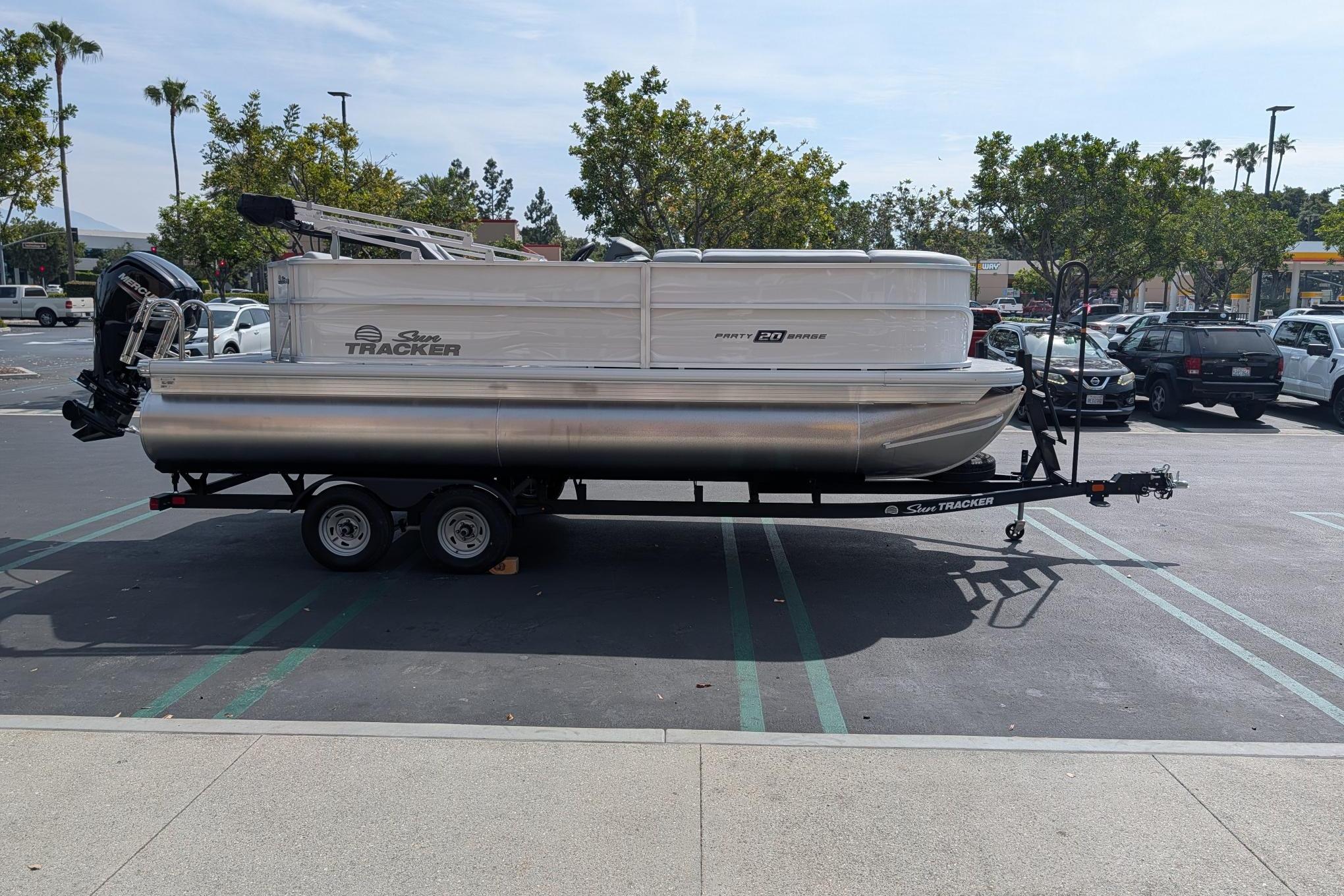 2026 Sun Tracker Party Barge 20 DLX pontoon boat on trailer in parking lot.