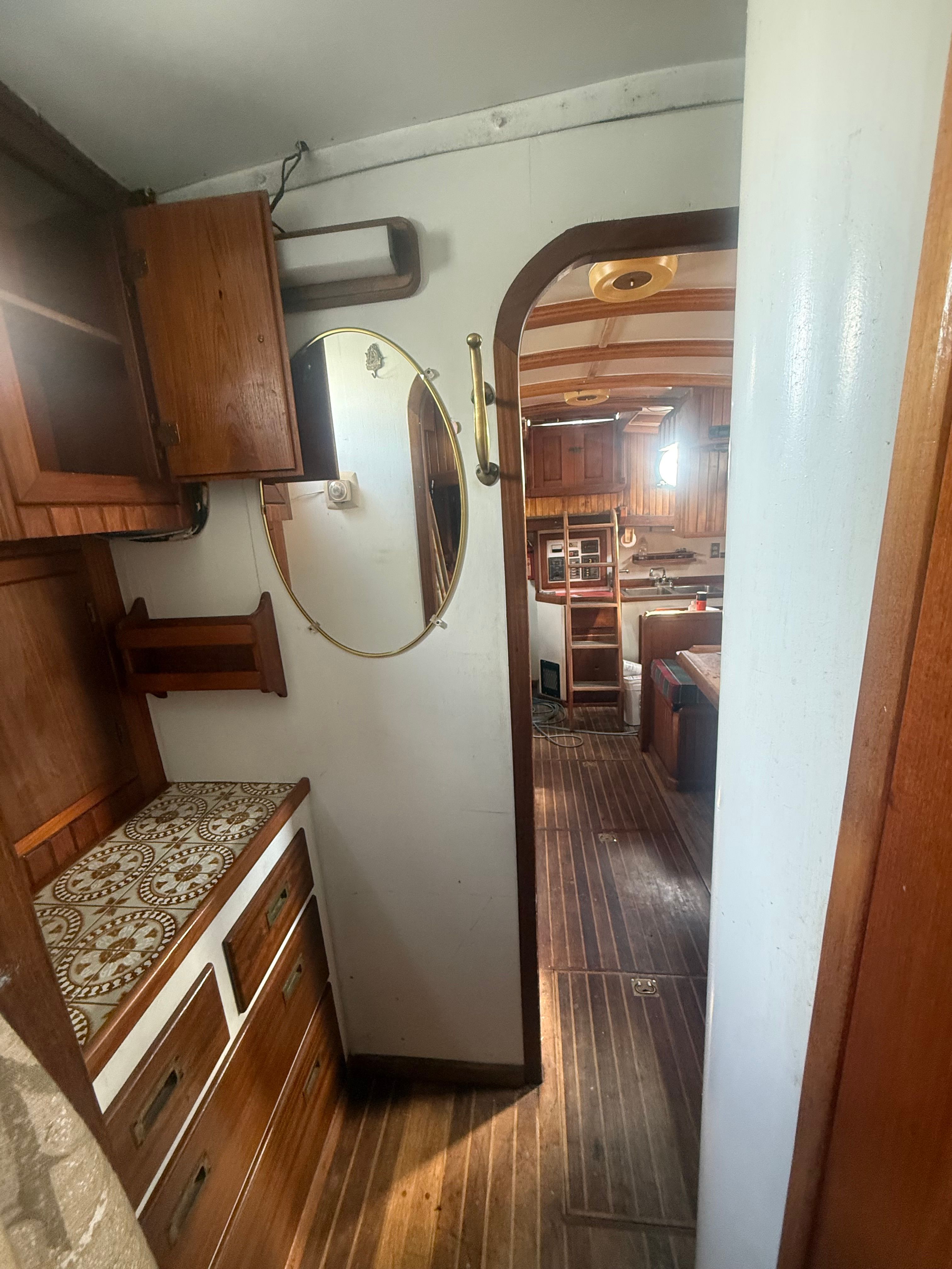 Interior of a classic sailboat with wooden furnishings and a round mirror.