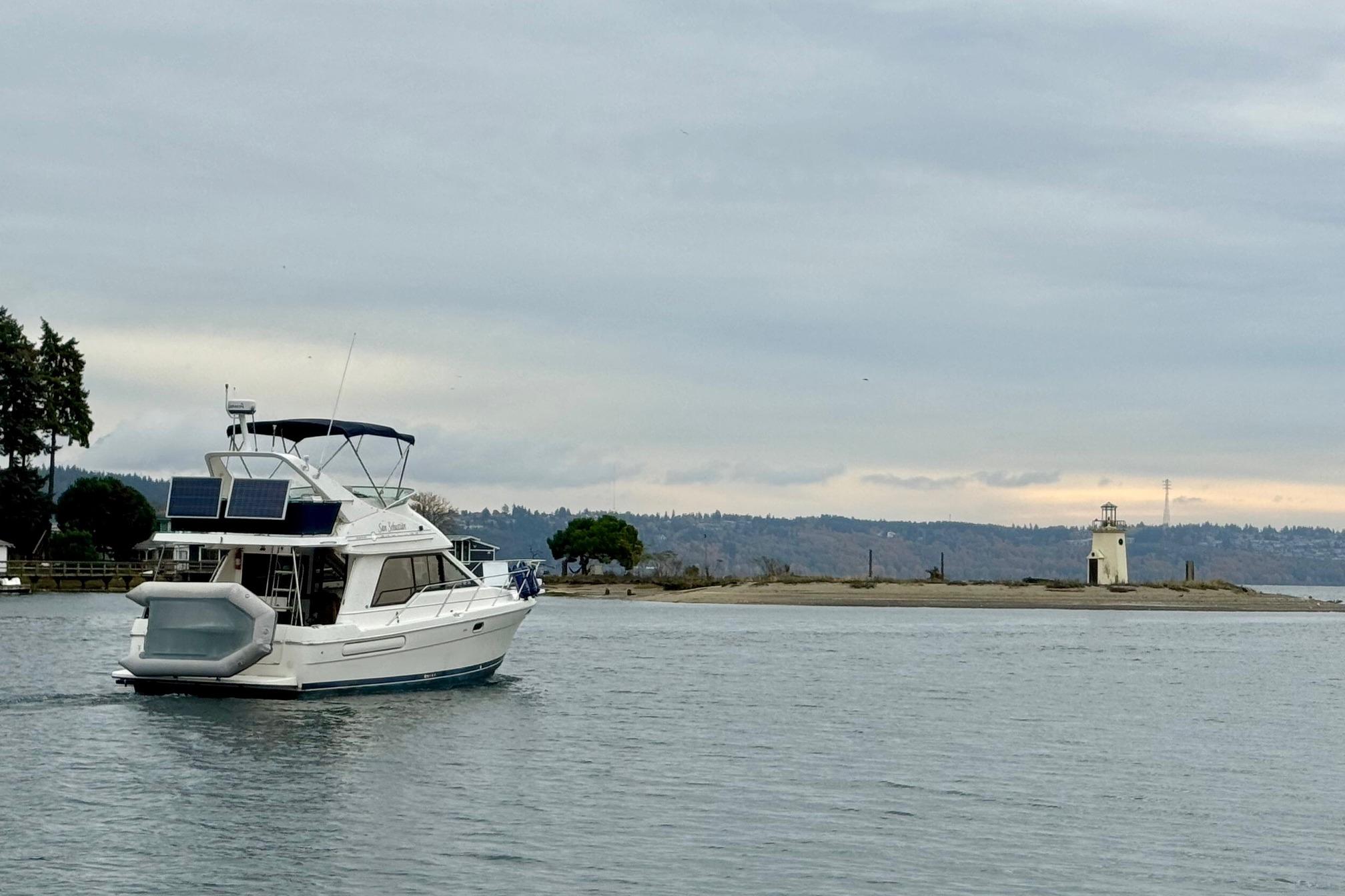 1998 Bayliner 3388 Command Bridge Motoryacht cruising near a lighthouse on a cloudy day.