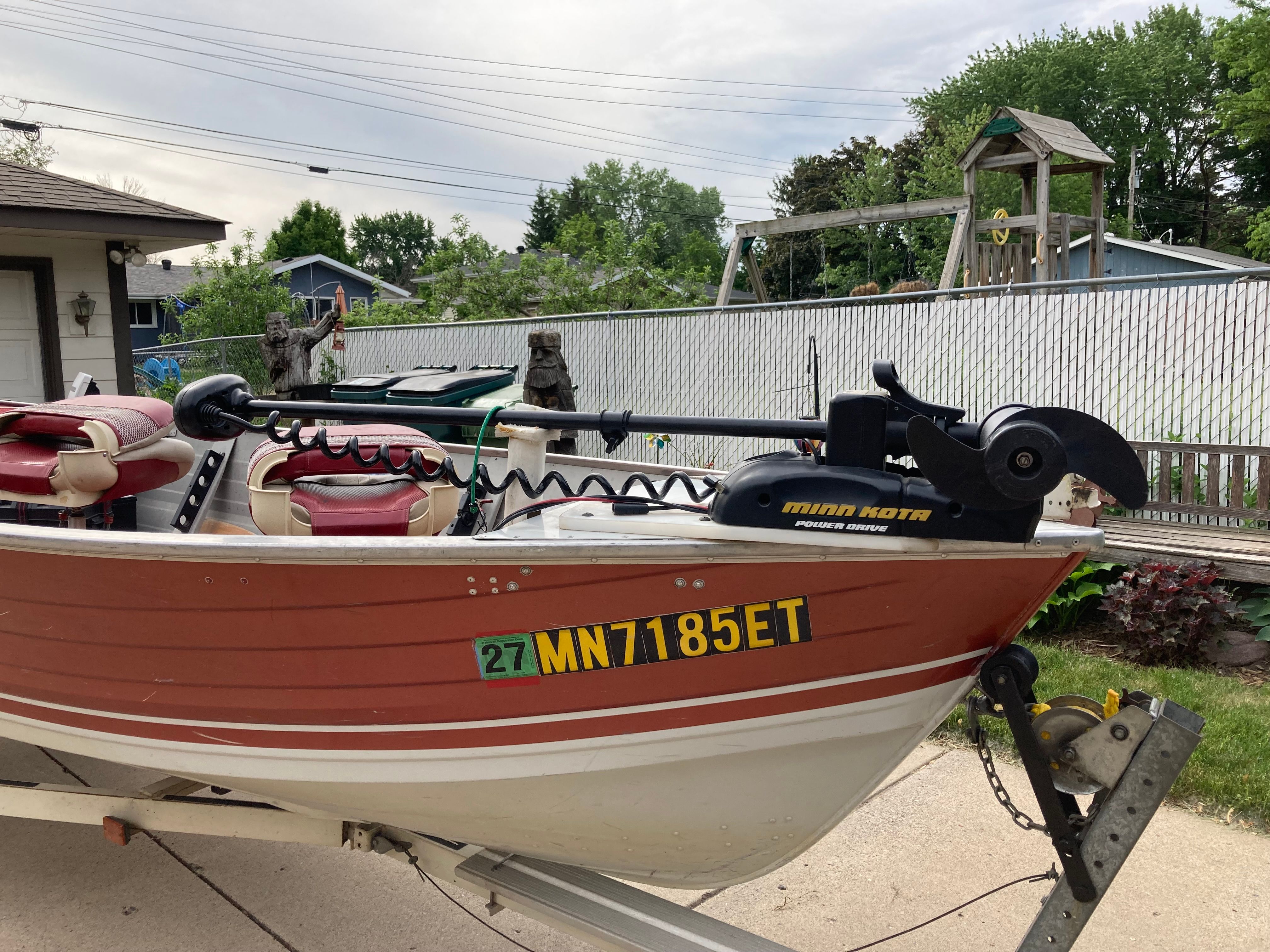 A red and white boat with seats and a Minn Kota motor on a trailer.
