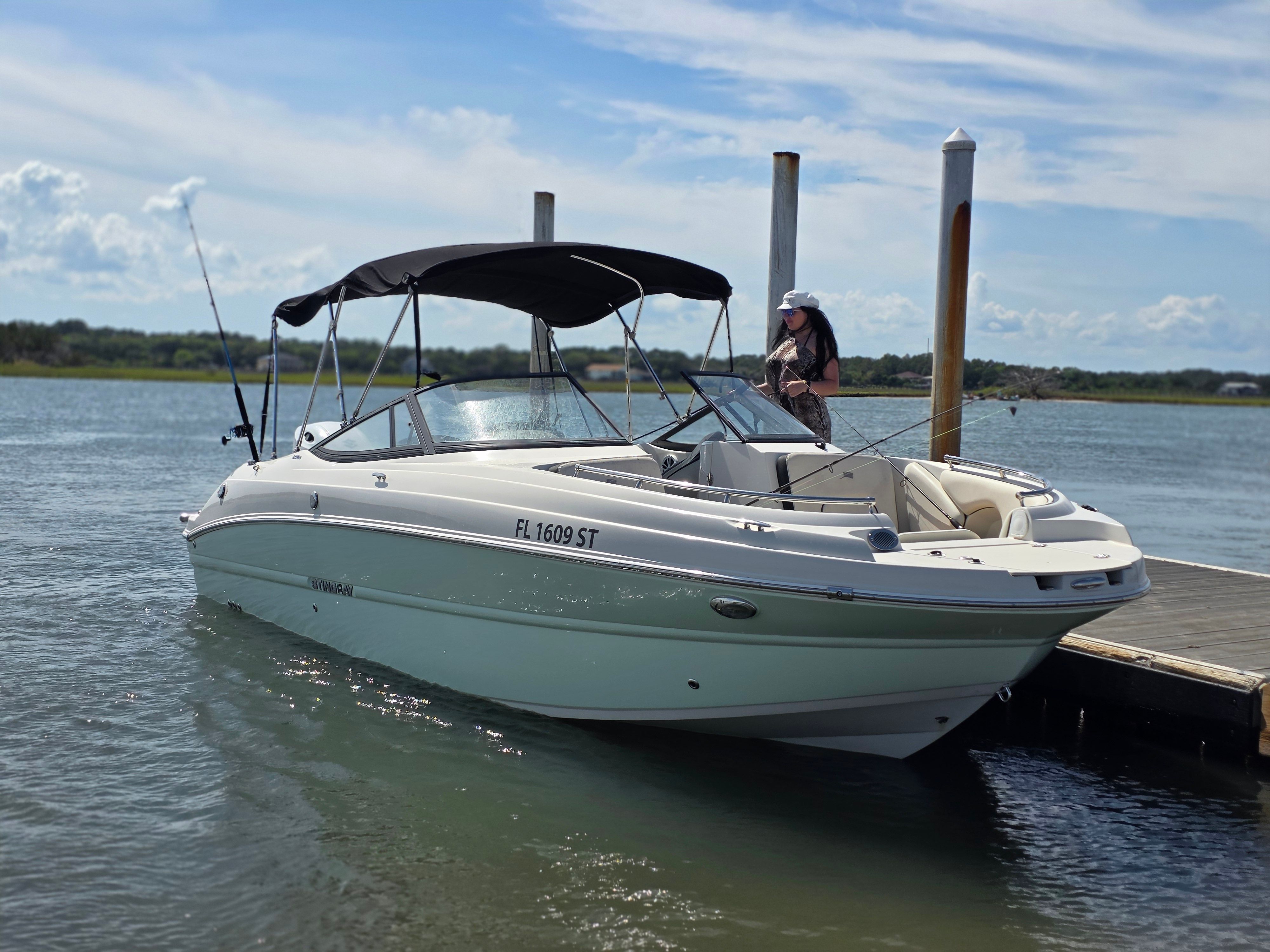 A white motorboat with a black canopy is docked at a wooden pier on the water.