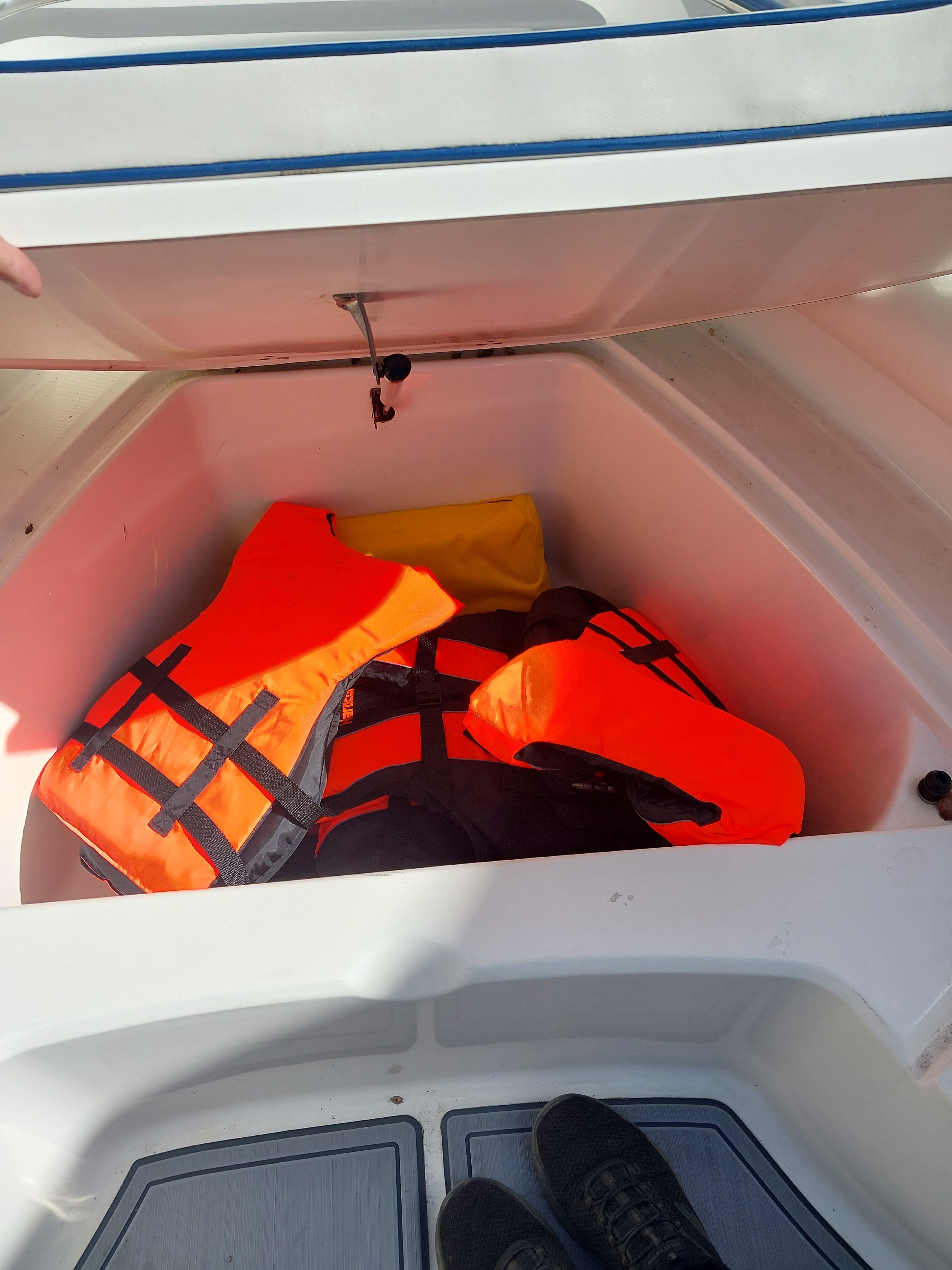 A storage compartment on a boat with several orange life jackets.