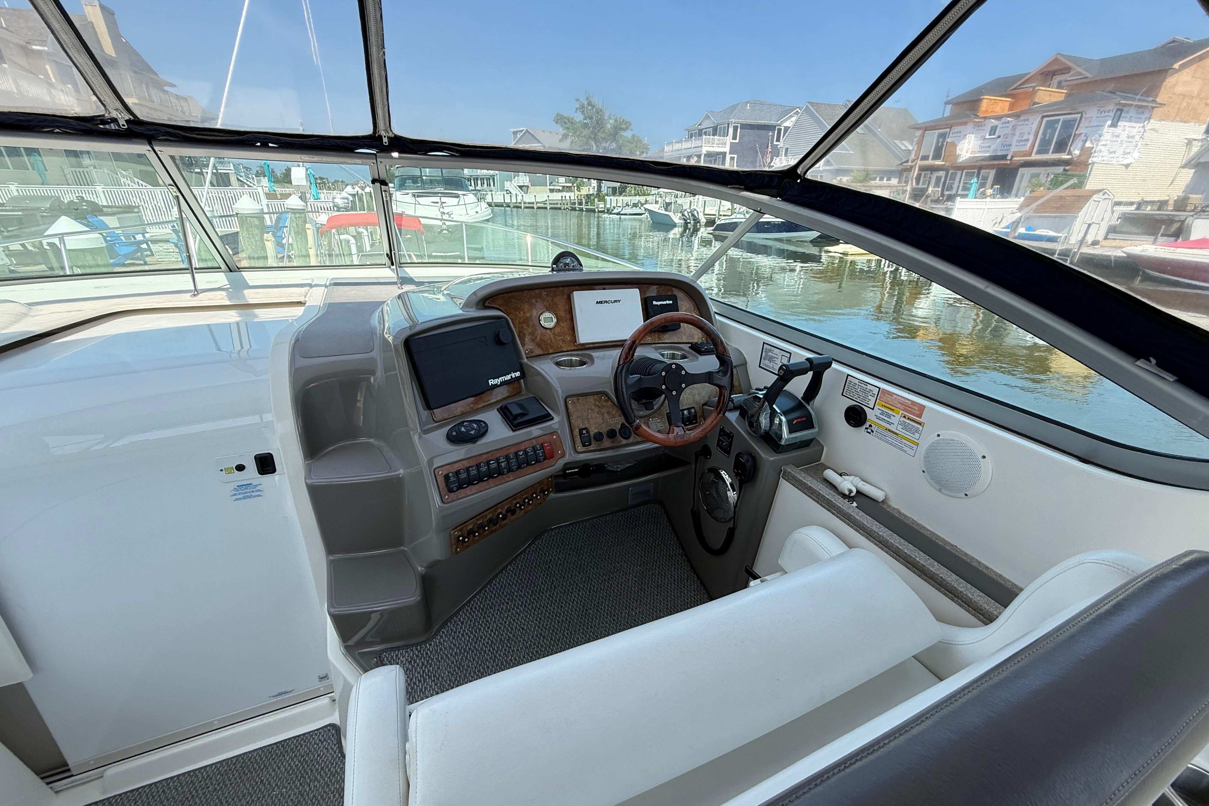 2009 Rinker 340 Express Cruiser cockpit with steering wheel, navigation system, and waterfront view.