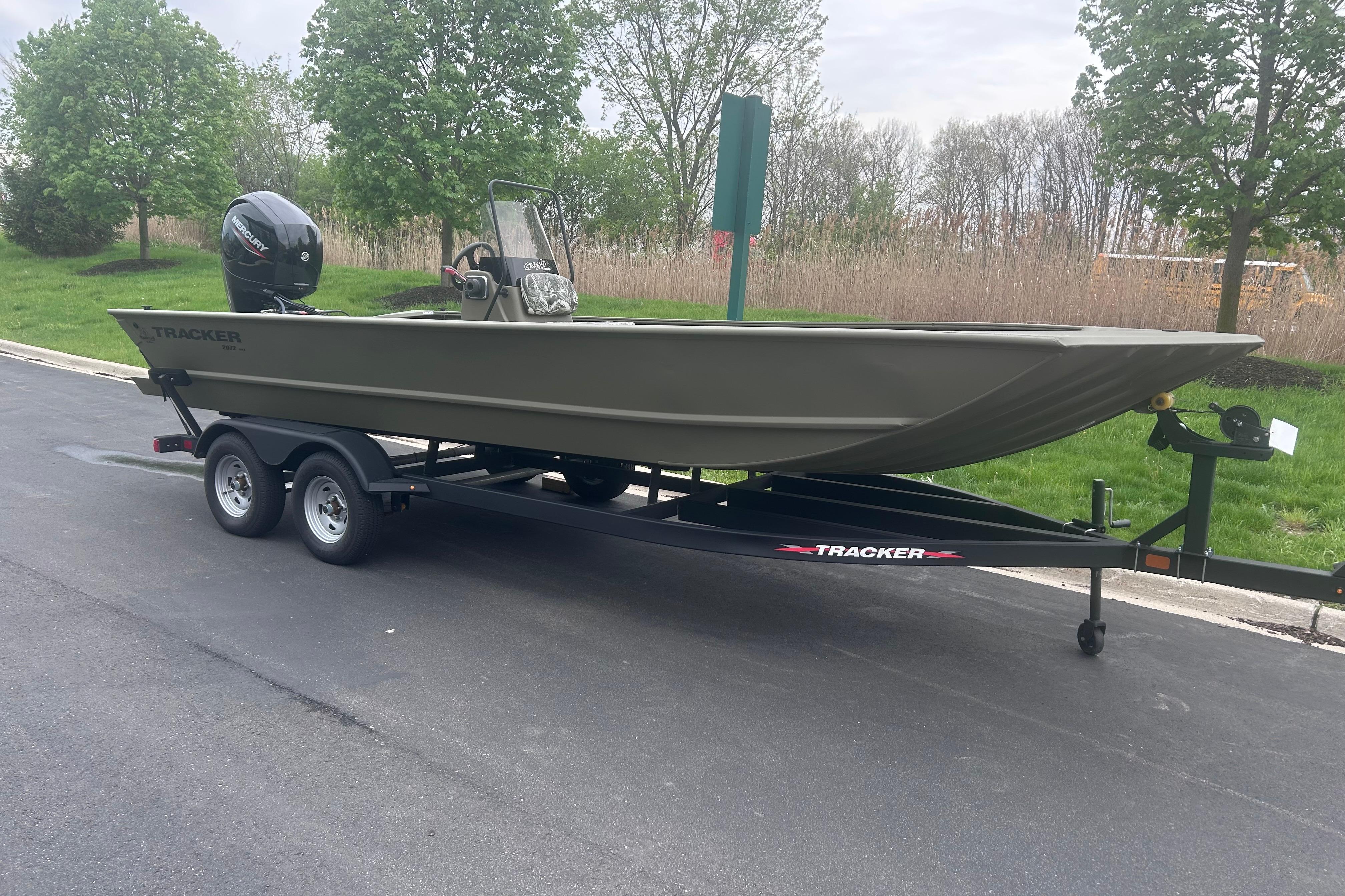 2024 Tracker Grizzly 2072 CC boat on trailer, parked outdoors with trees in background.