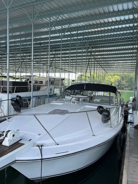 A white boat docked in a covered marina, featuring black fenders and a black canopy.