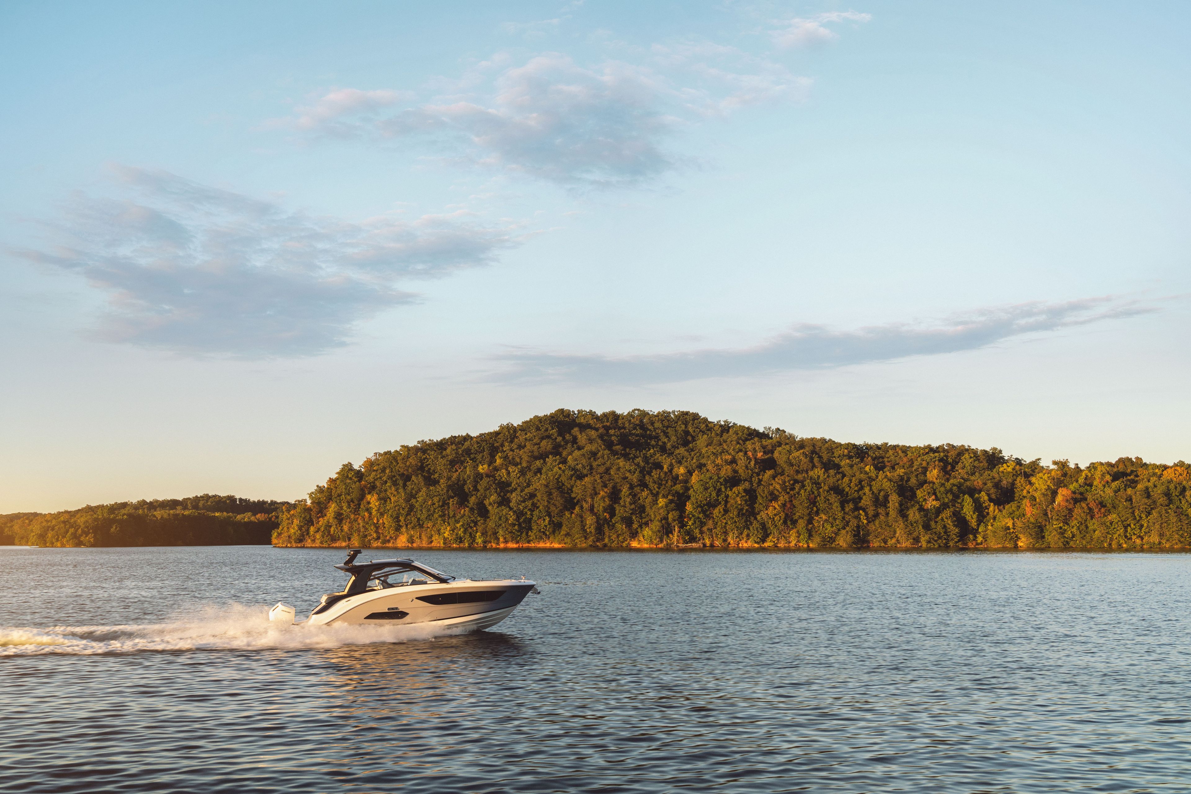 A Sea Ray Sundancer 370 Outboard cruising on calm waters with a wooded island in the background.