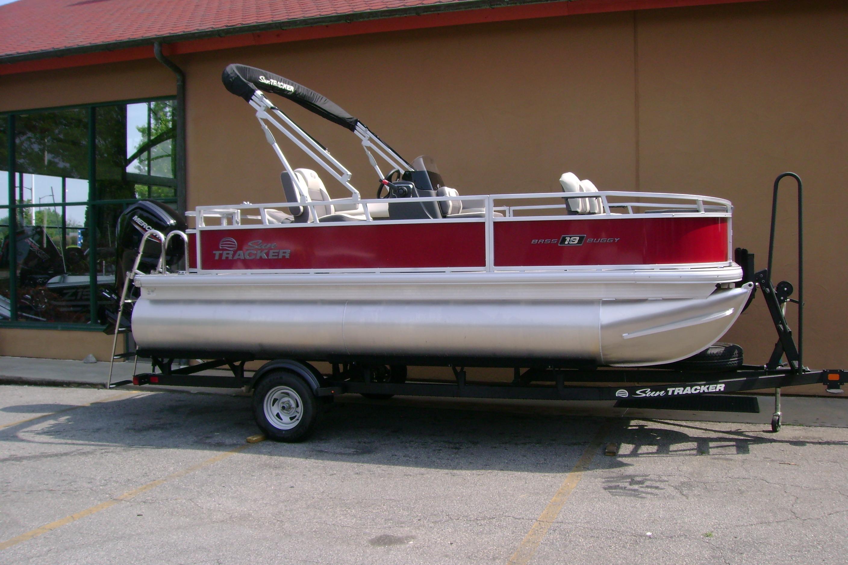 2026 Sun Tracker Bass Buggy 18 DLX pontoon boat on trailer, parked outside a building.