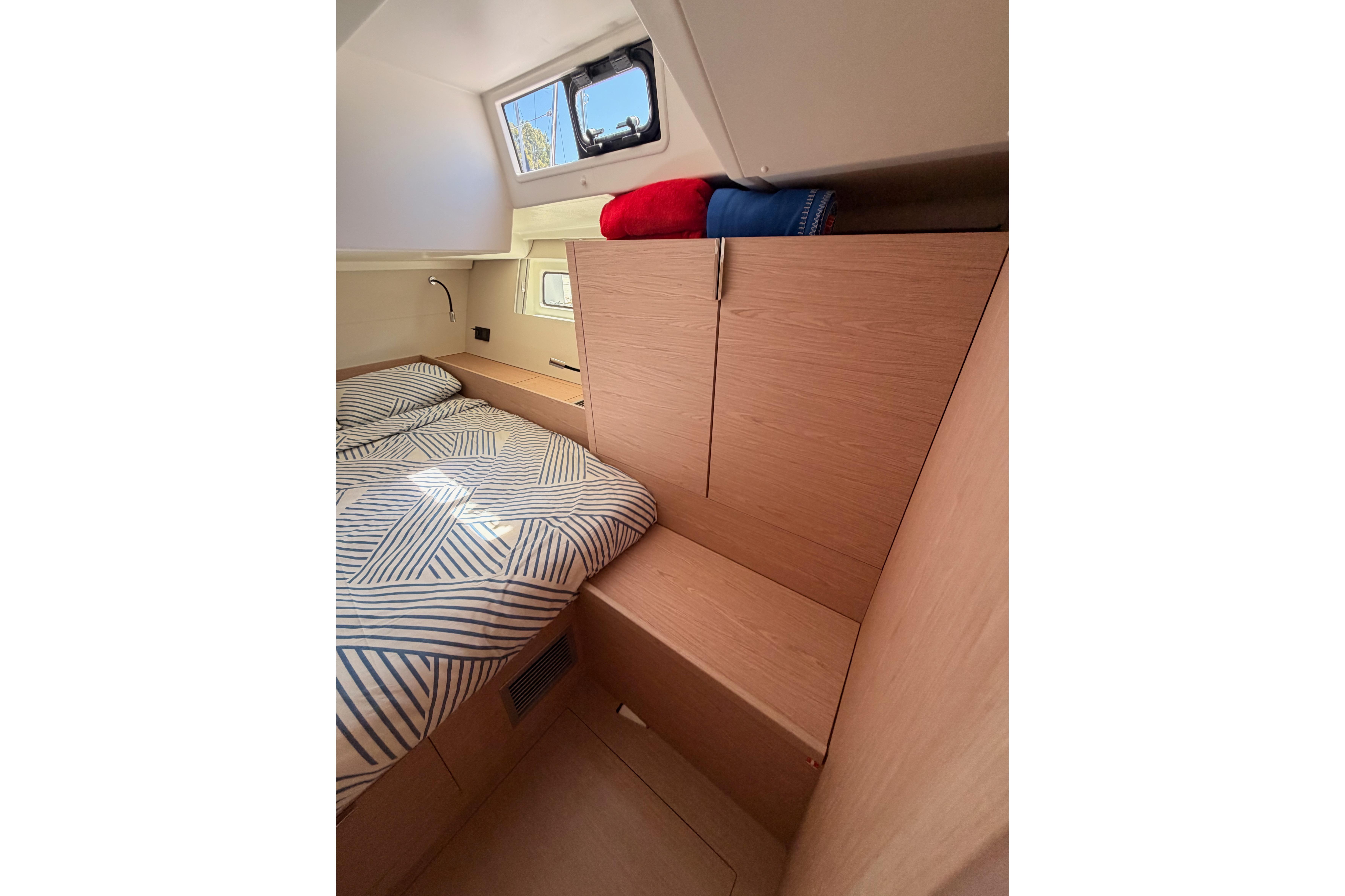 Interior cabin of 2022 Beneteau Oceanis Yacht 54 with striped bedding and wooden cabinetry.