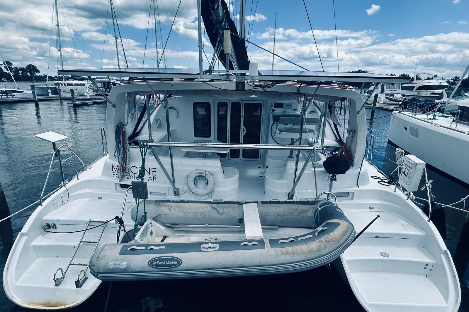 2001 Robertson & Caine Leopard catamaran docked with inflatable dinghy, under a partly cloudy sky.