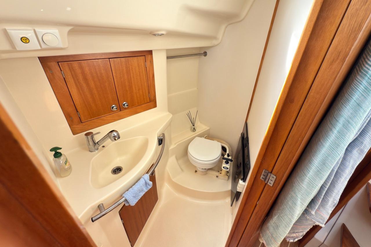 Compact bathroom in 2006 Elan Impression 384 yacht with sink, toilet, and wooden cabinetry.
