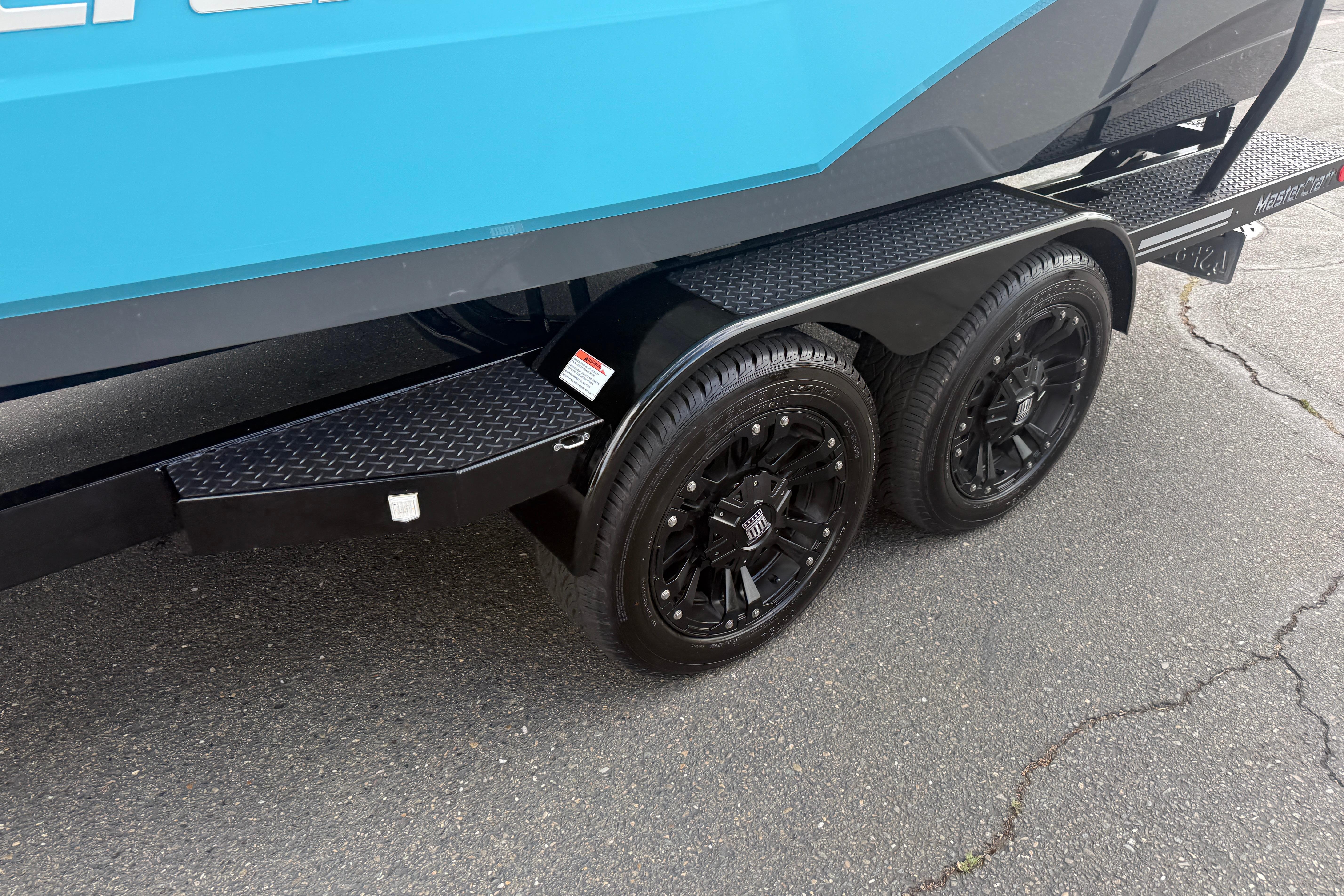 2018 MasterCraft XT21 trailer with black wheels and blue hull on pavement.