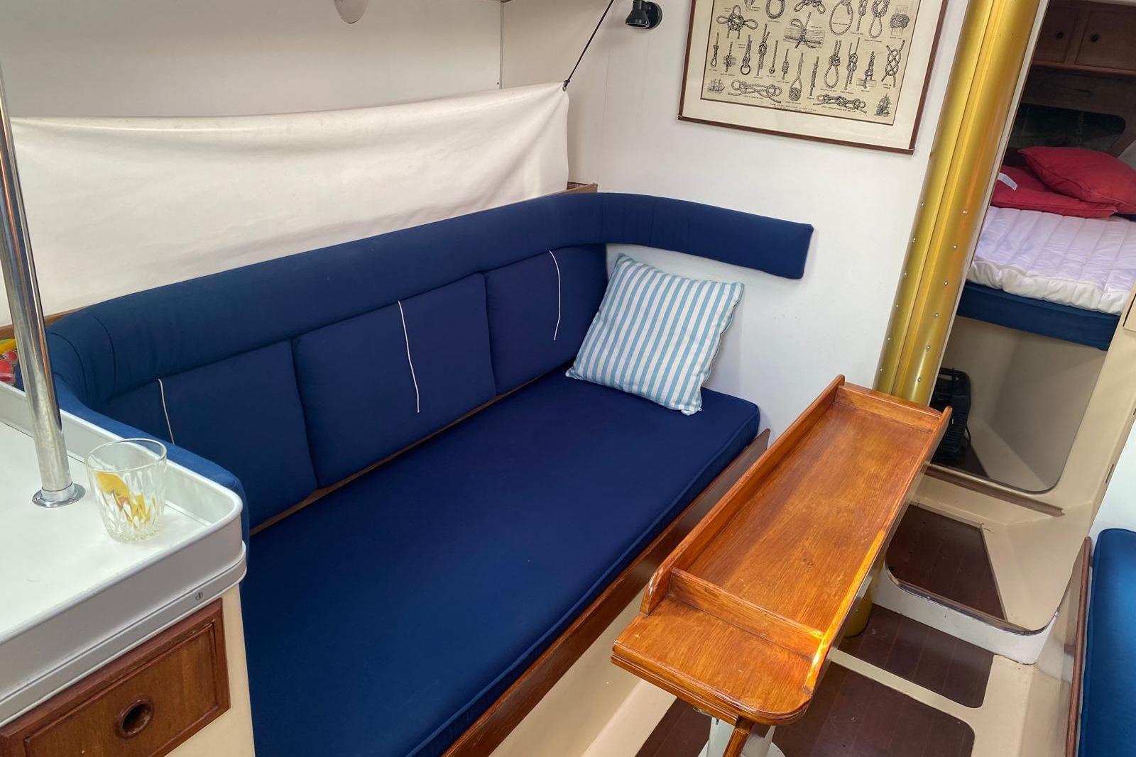 Cozy interior of a 1977 Nicholson 31 sailboat with blue seating and wooden table.