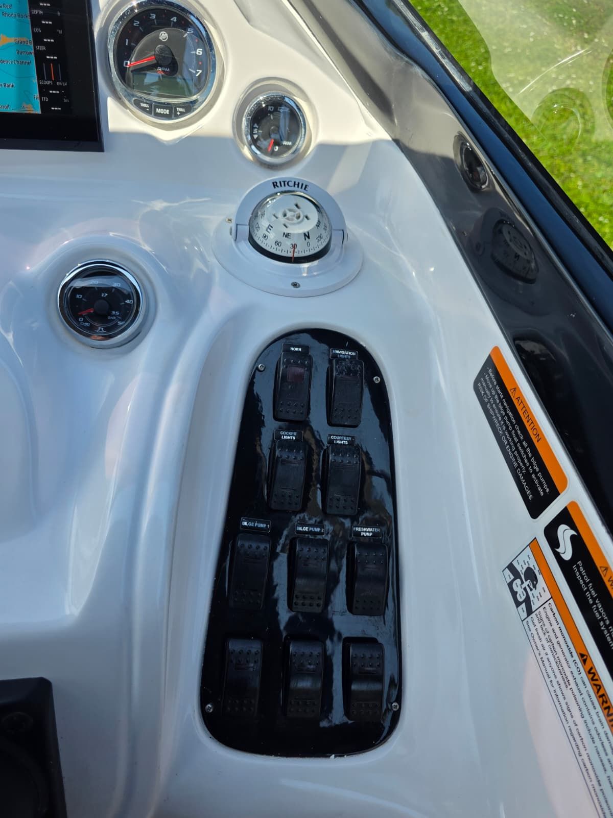 The image shows a boat dashboard with various instruments and switches.