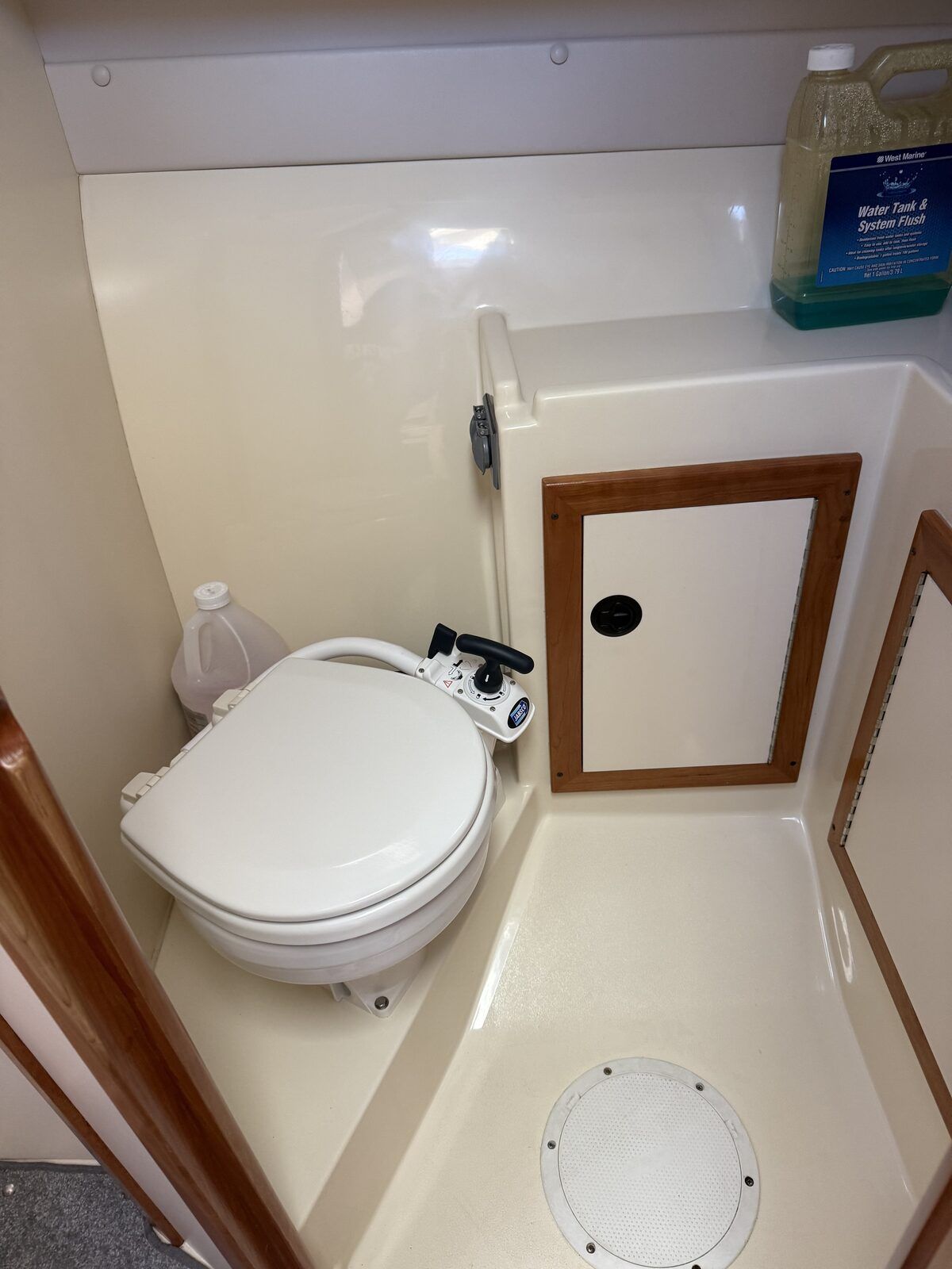 Small bathroom on a boat with a toilet and cleaning supplies.