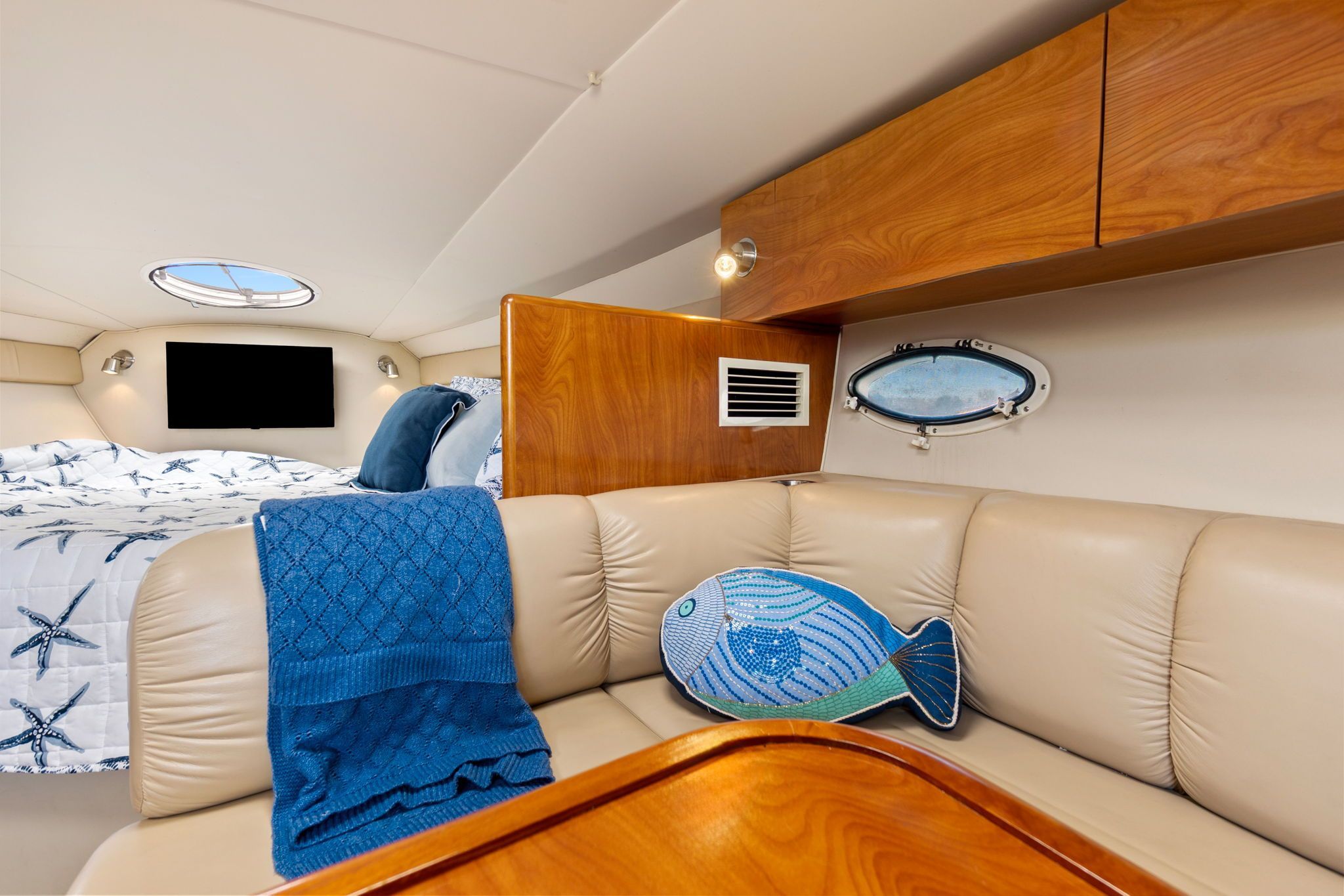 Interior of a 2007 Larson Cabrio 330 with beige sofa, blue blanket, and fish pillow.