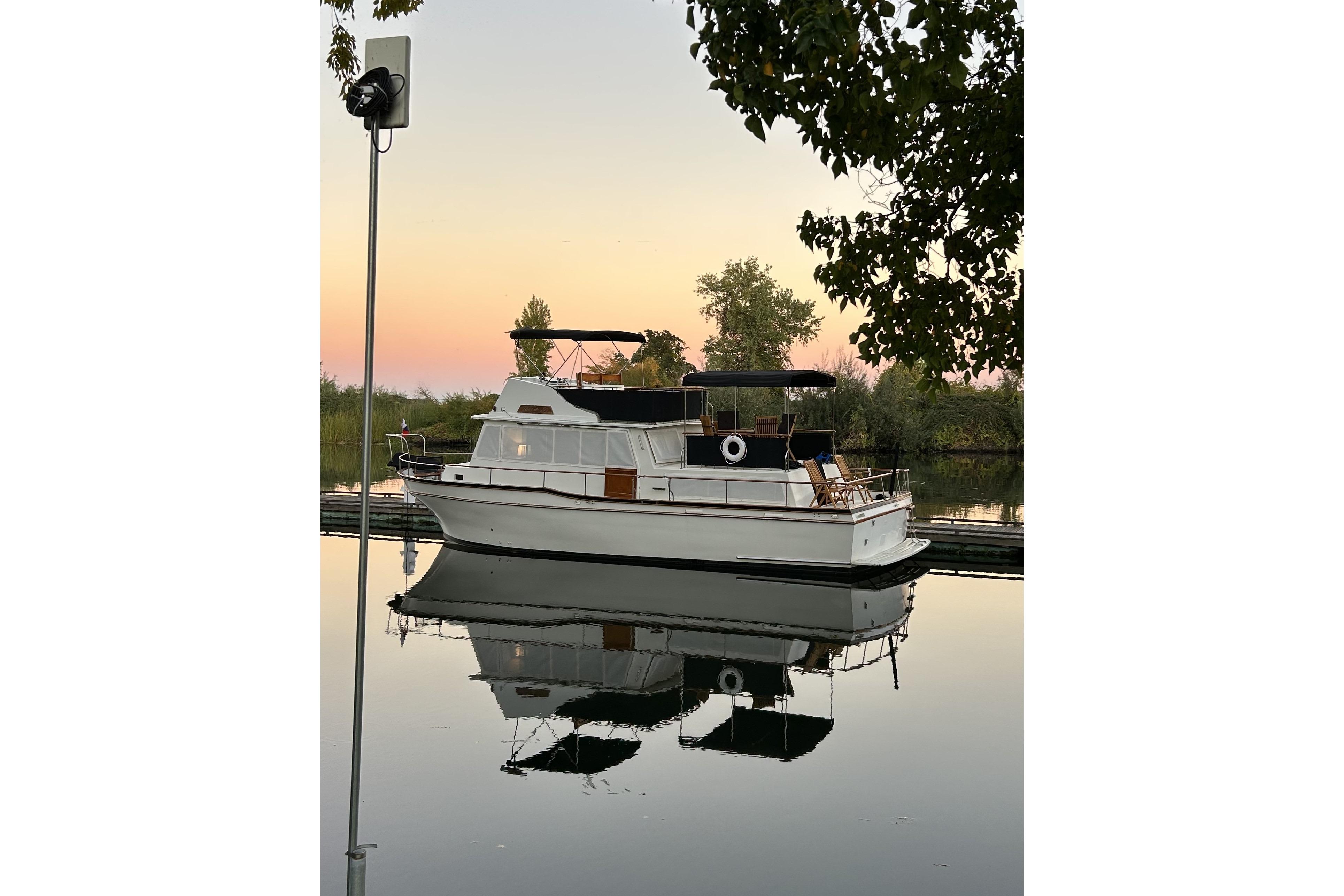 1978 Californian 42 LRC yacht on calm water at sunset, reflecting trees and sky.