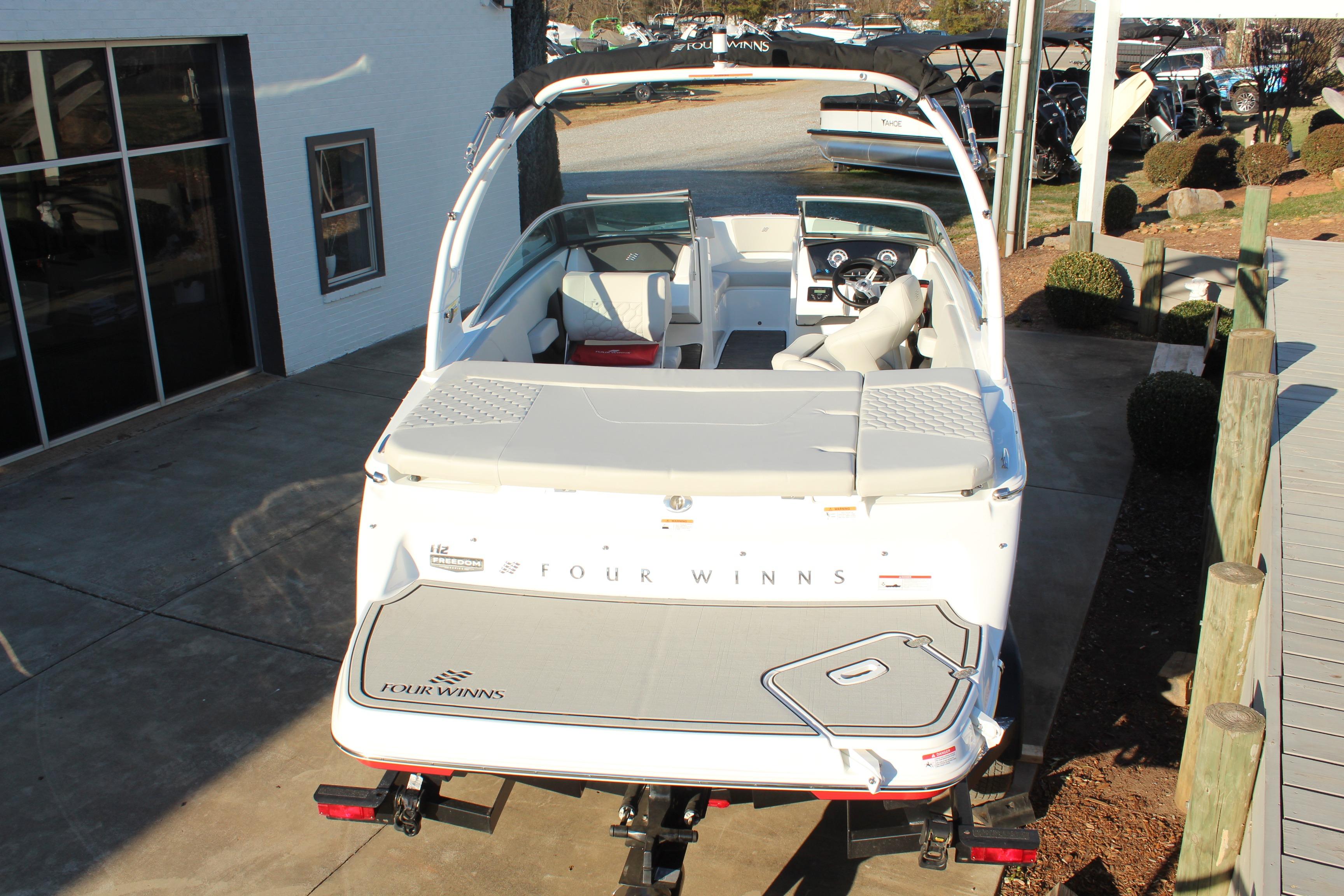 2026 Four Winns H2 Freedom boat, rear view, parked on a trailer near a building.