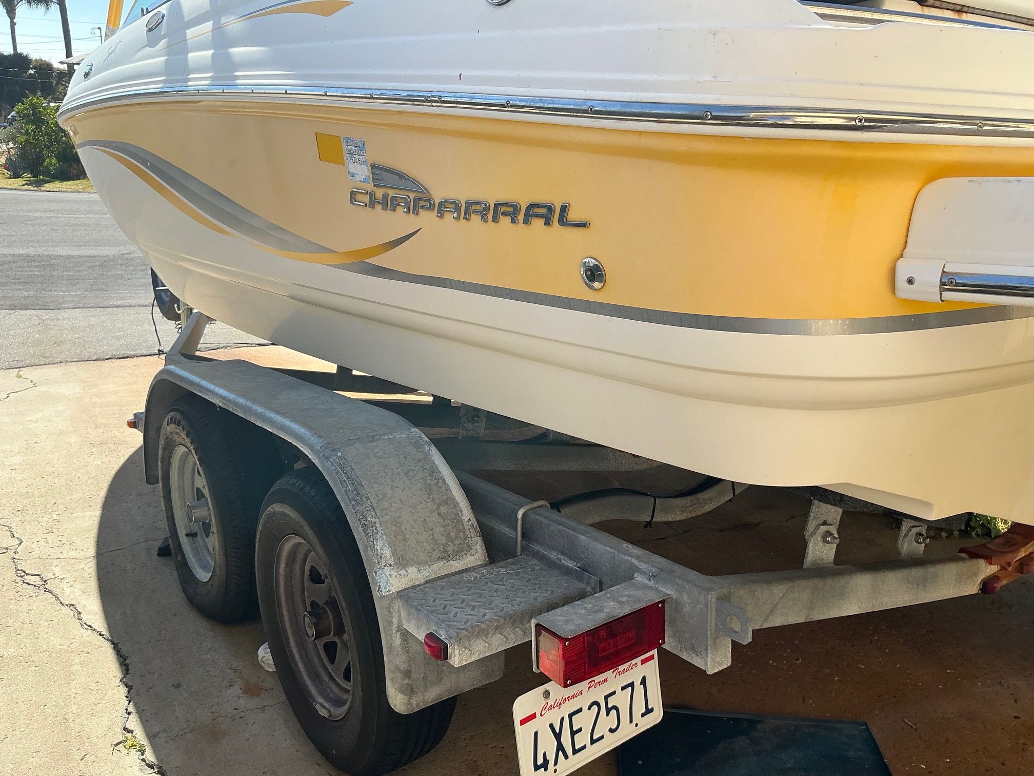 A yellow 2003 Chaparral 210 SS boat is on a trailer in a driveway.