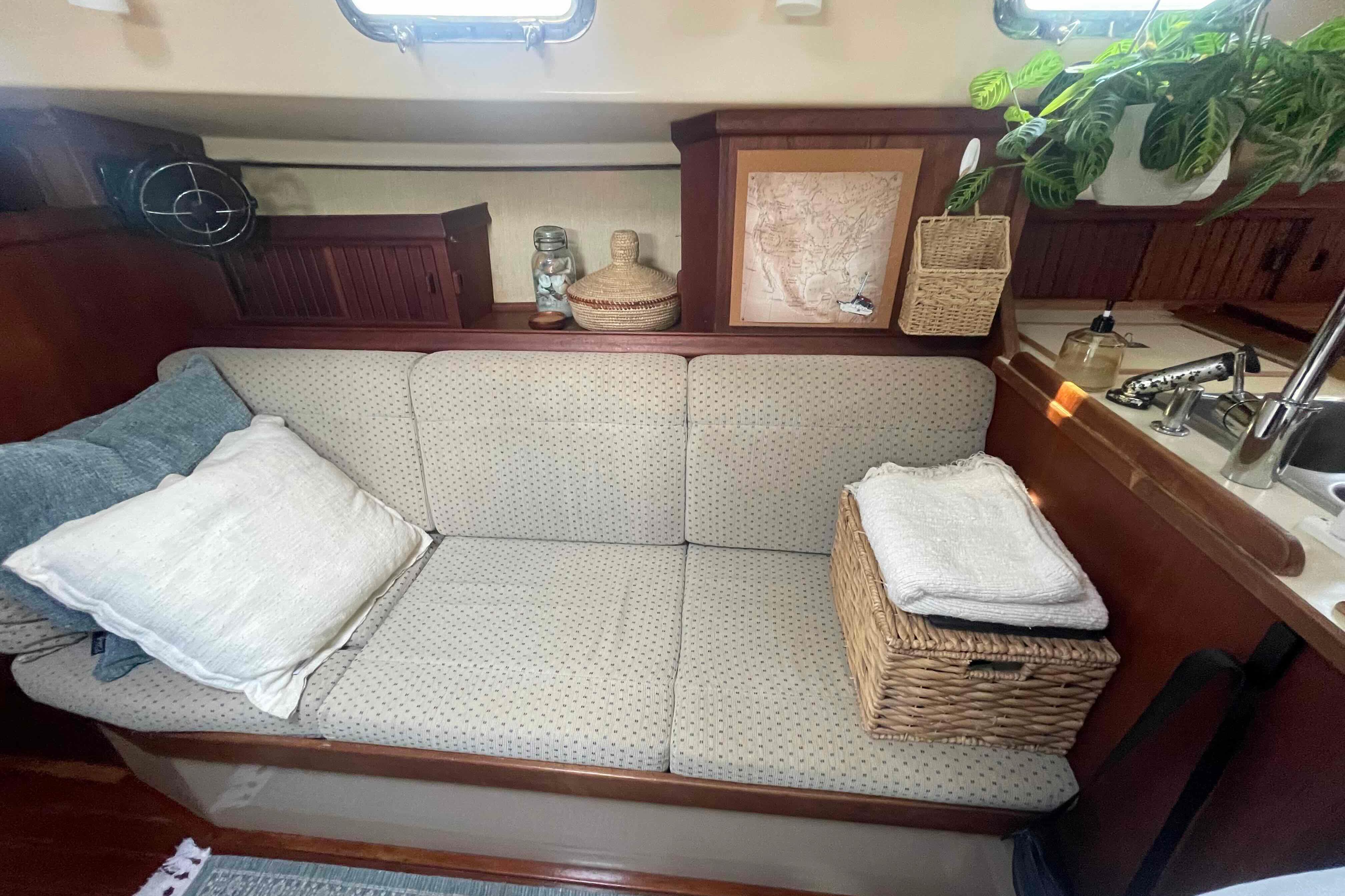 Cozy interior of 1989 Island Packet 35 sailboat with cushioned seating and wicker basket.